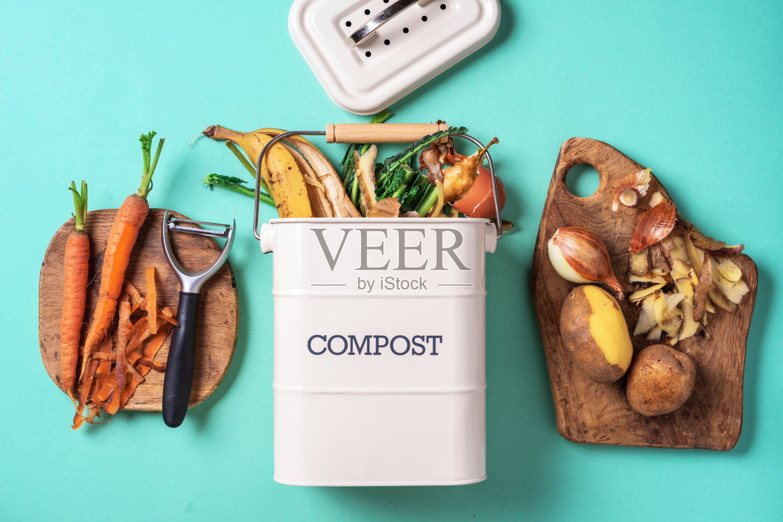 俯视图厨房的食物垃圾收集在回收堆肥锅。去皮的蔬菜在切菜板,白色的堆肥箱在蓝色的背景。照片摄影图片