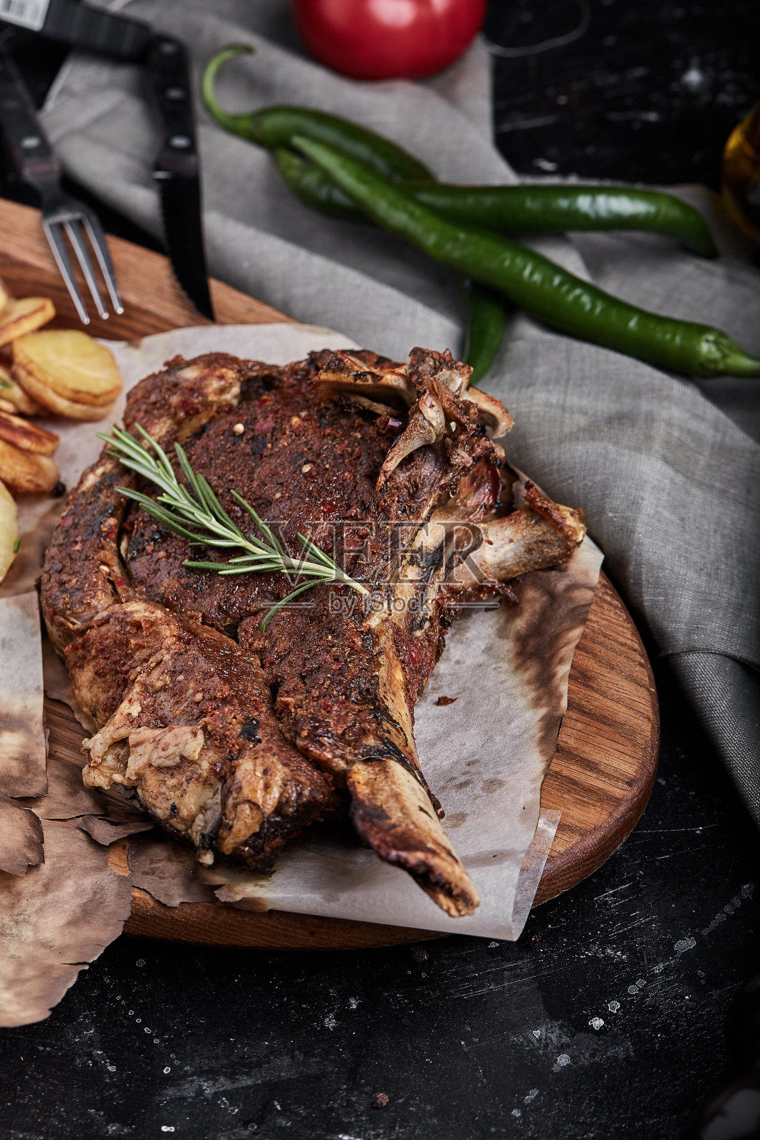 战斧牛排,蔬菜和刀放在桌上。桌上有烤肉、烤蔬菜和新鲜蔬菜照片摄影图片