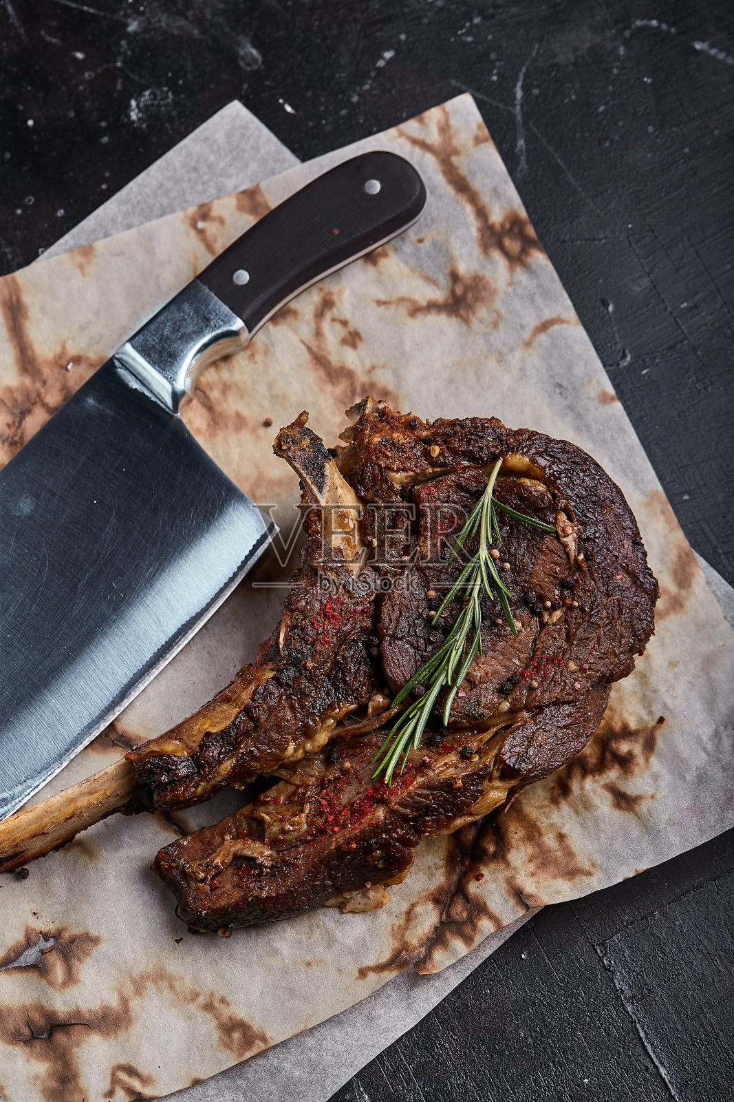 战斧牛排,蔬菜和刀放在桌上。桌上有烤肉、烤蔬菜和新鲜蔬菜照片摄影图片