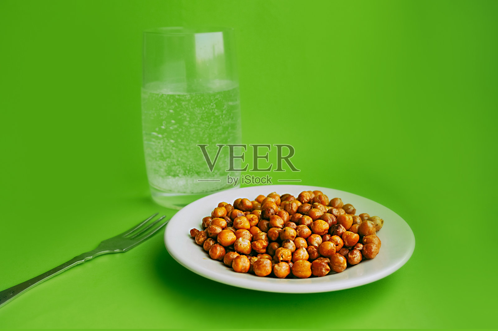 为健康食品。准备好的鹰嘴豆和一杯纯净的苏打水,在干净的绿色背景下,用一个老式的灰色叉子。照片摄影图片