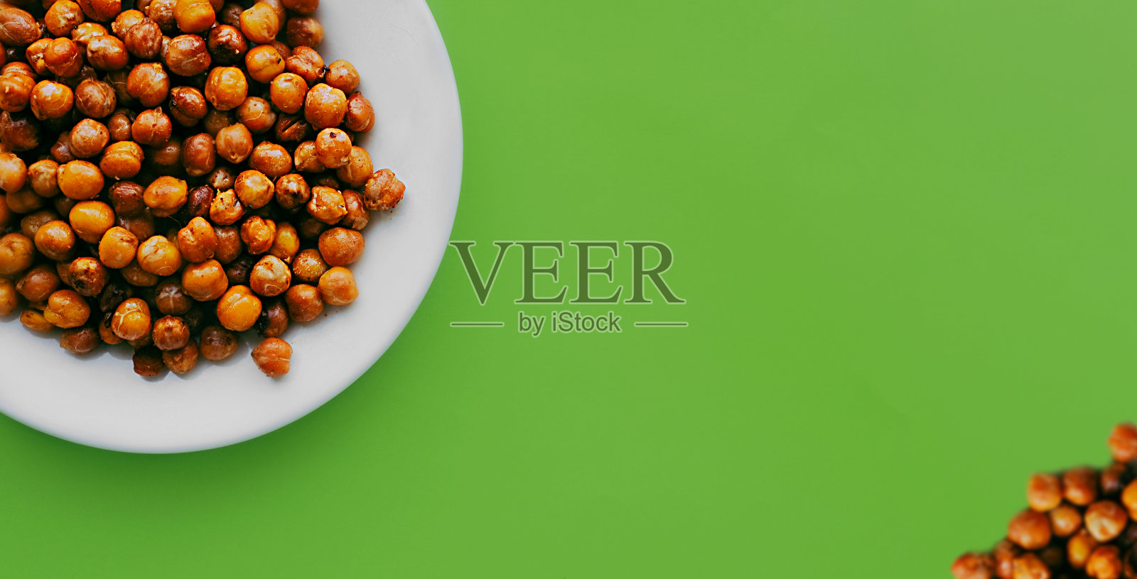 健康饮食的旗帜。在干净的绿色背景下,在白色的盘子里放上炒好的鹰嘴豆。照片摄影图片