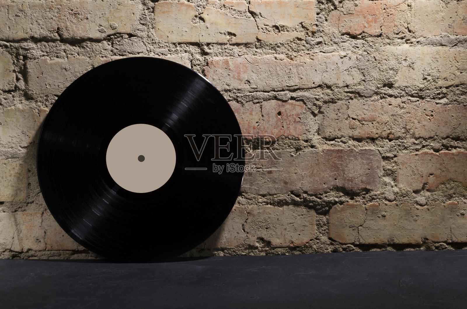 黑旧的黑胶唱片贴着质朴的砖墙,放在黑色的桌子上。夜总会派对的概念。设计空间照片摄影图片