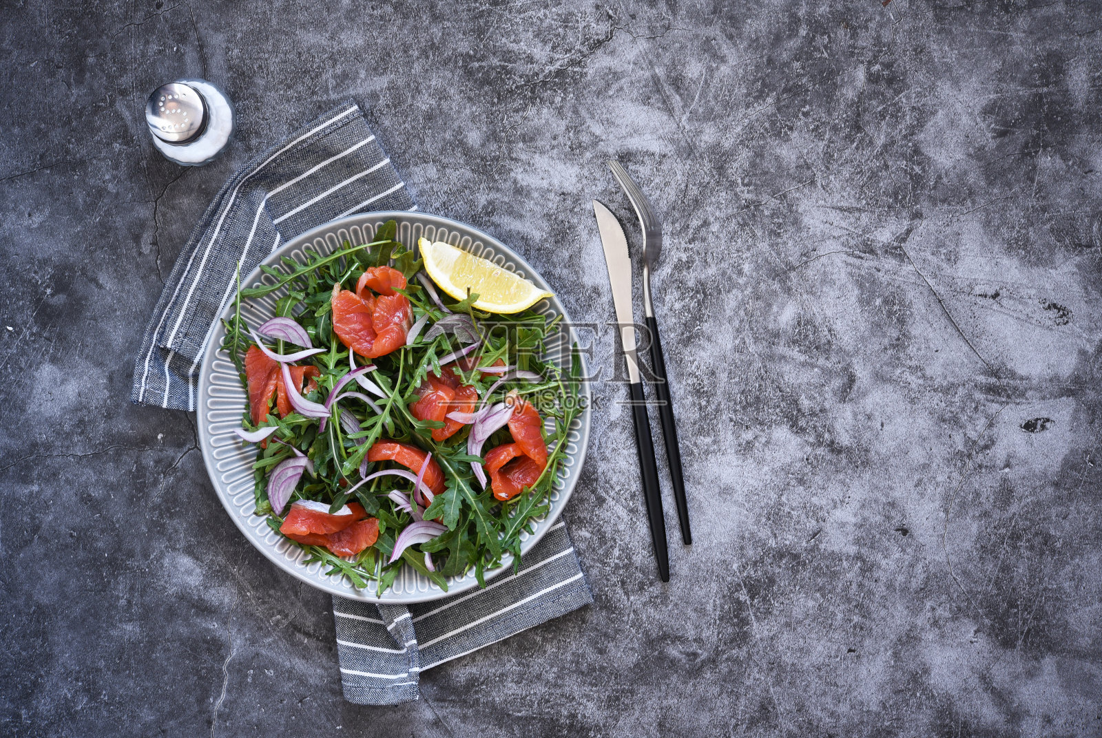 厨房昏暗的桌子上放着芝麻菜和鲑鱼沙拉。带有文本位置的俯视图。照片摄影图片