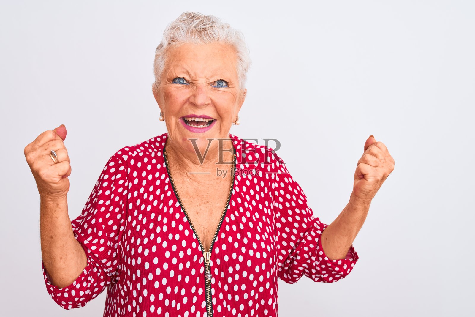 年长的白人女子身穿红色休闲夹克,在白色背景前非常高兴和兴奋,举起双臂做出胜利者的姿势,面带微笑,为成功欢呼。庆祝概念照片摄影图片