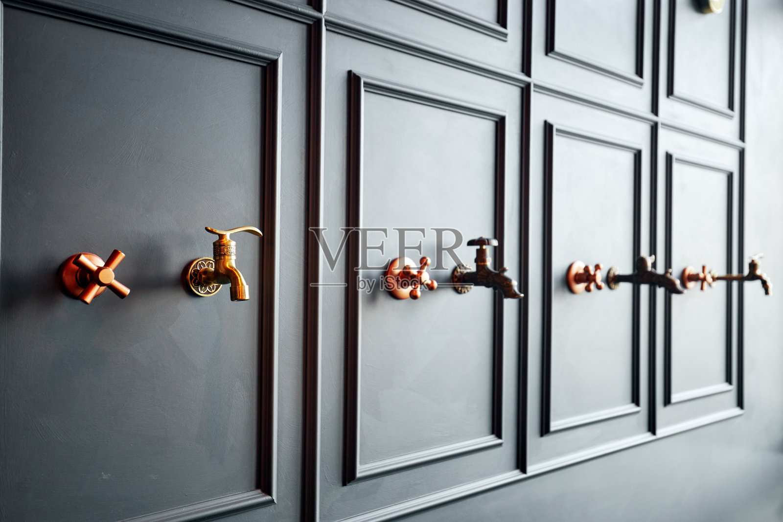 灰色的墙上挂着一排排不同的青铜水龙头照片摄影图片