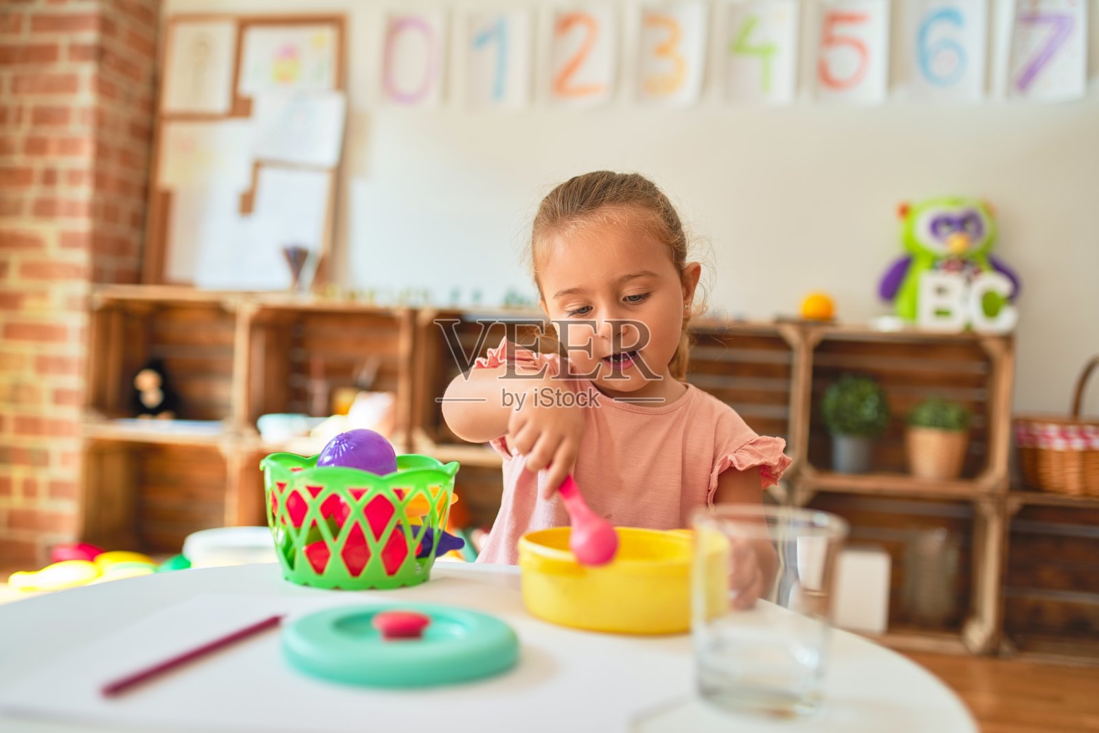 金发碧眼的蹒跚学步的小女孩在幼儿园用塑料食品玩饭照片摄影图片
