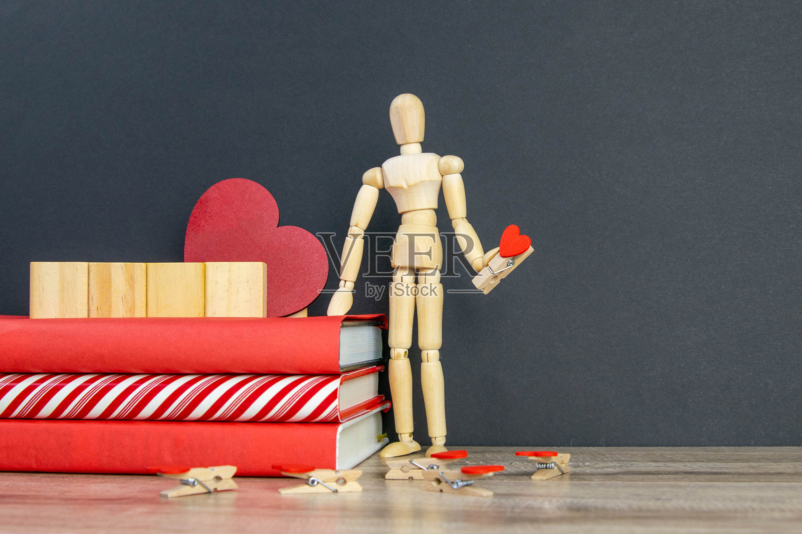 一堆红色的书,上面有四个木方,旁边有一个木制的人,手里拿着一枚心形的别针照片摄影图片