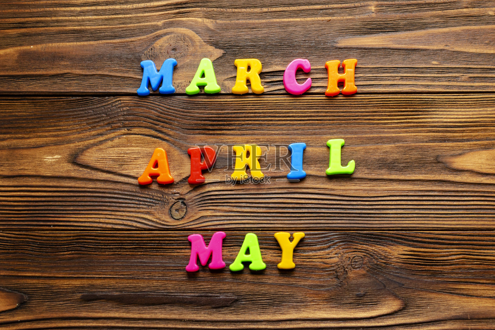 木制背景上的彩色塑料磁铁上写着“三月,四月,五月”照片摄影图片