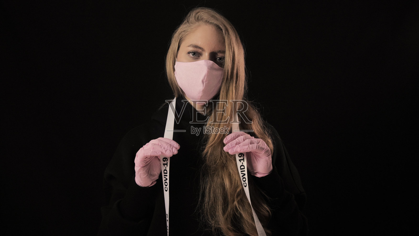 戴粉色口罩的女孩拿着写有COVID-19的胶带。隔离在黑色背景上。医疗保健概念。4k。冠状病毒疾病,疫情,大流行照片摄影图片