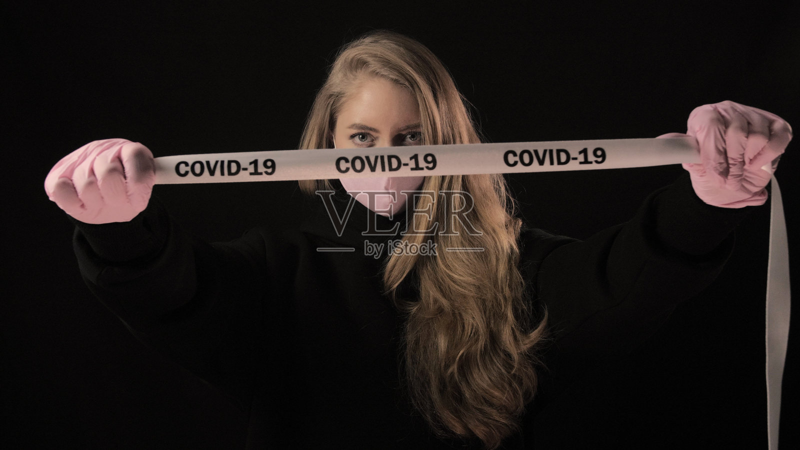 戴粉色口罩的女孩拿着写有COVID-19的胶带。隔离在黑色背景上。医疗保健概念。4k。冠状病毒疾病,疫情,大流行照片摄影图片
