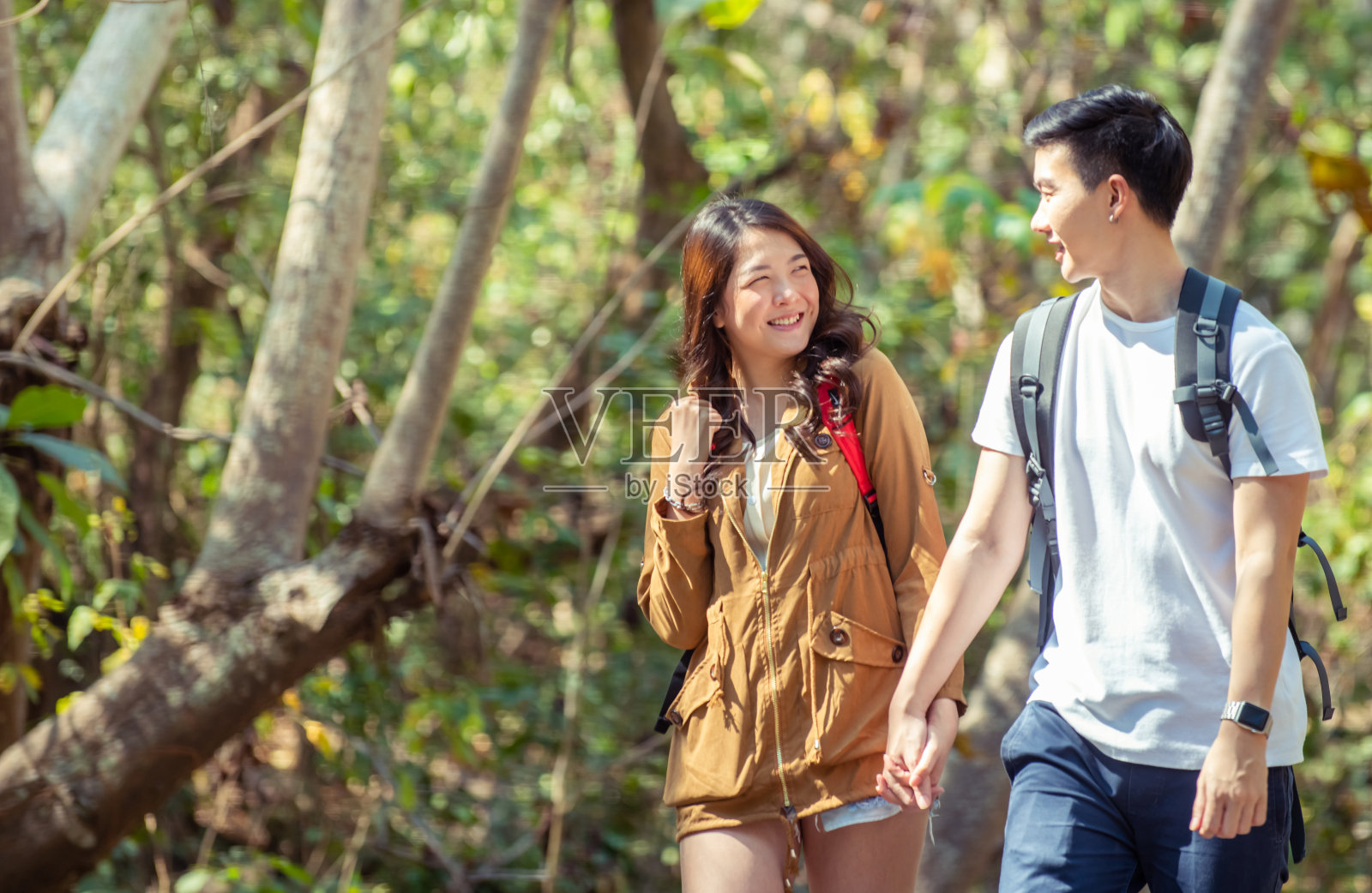 快乐的年轻亚洲夫妇男人和美丽的女人肩并肩在森林里徒步旅行微笑和互相看着对方。男朋友和女朋友在玩暑假照片摄影图片