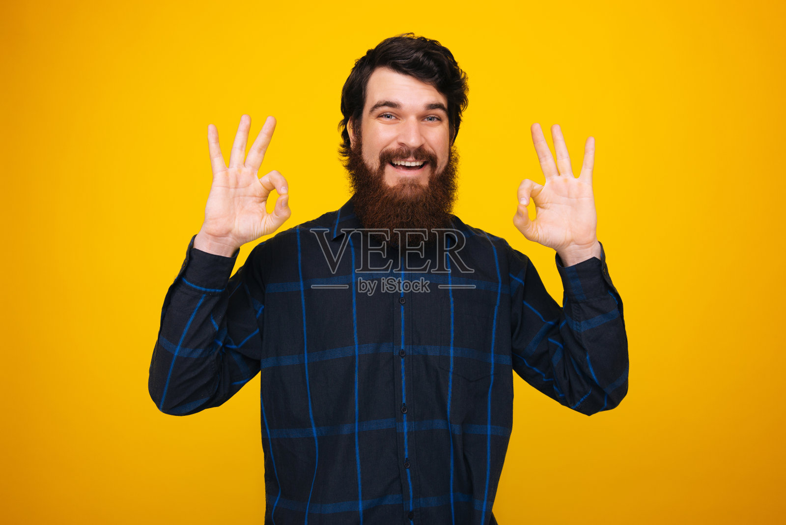 英俊的胡子男子做出ok手势与双手在黄色的背景。照片摄影图片