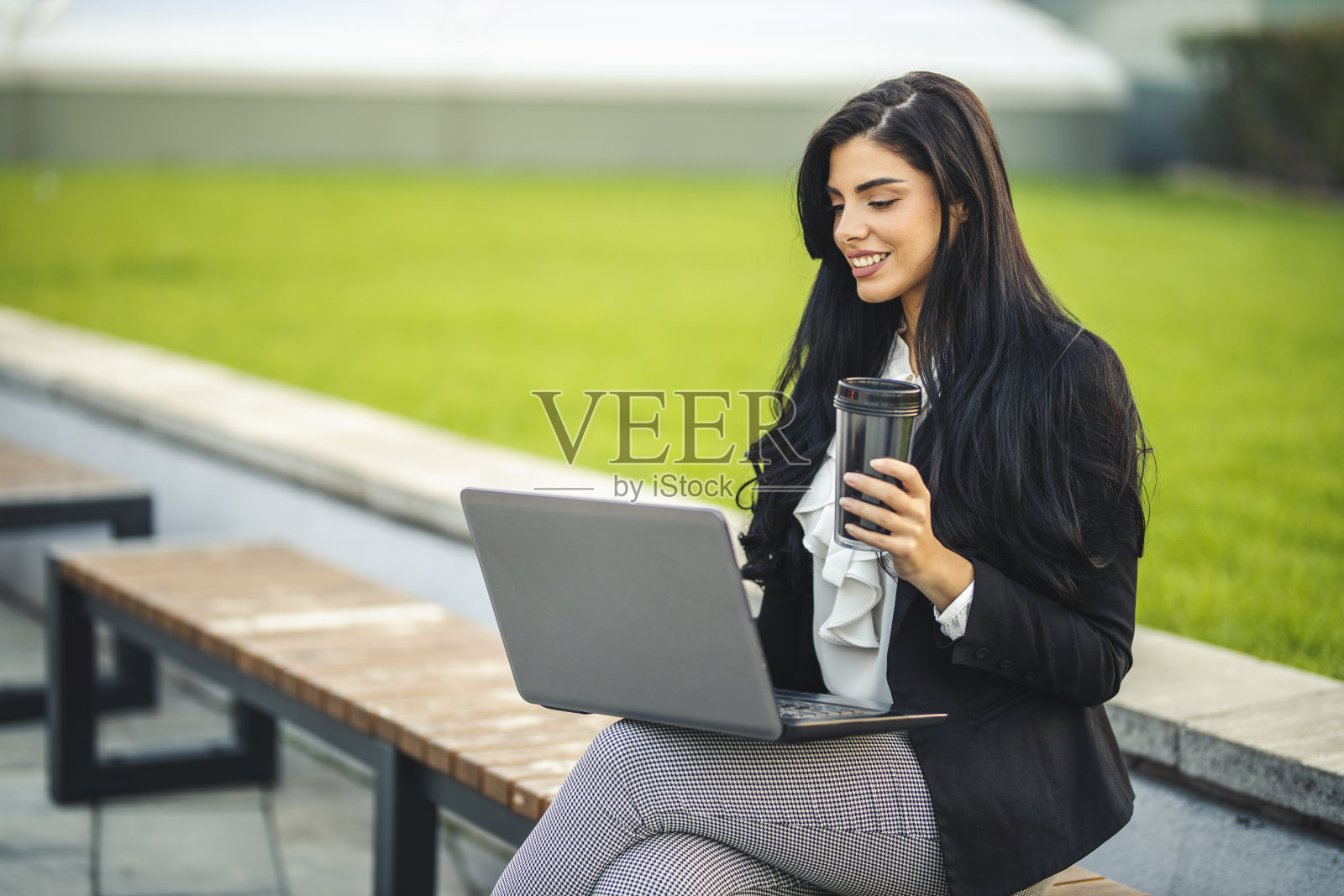 在公园长椅上用笔记本电脑喝咖啡的女商人照片摄影图片