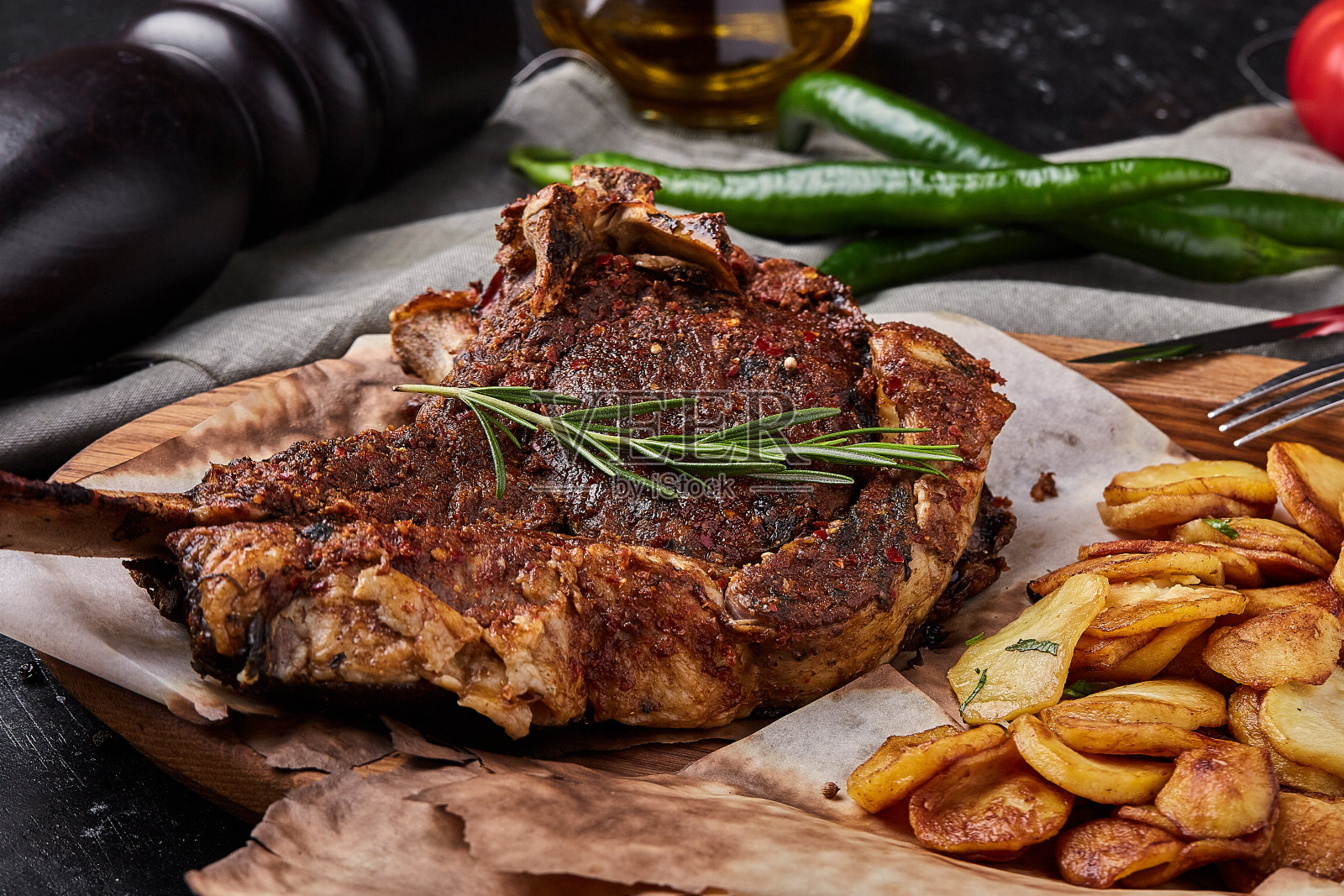 战斧牛排,蔬菜和刀放在桌上。桌上有烤肉、烤蔬菜和新鲜蔬菜照片摄影图片