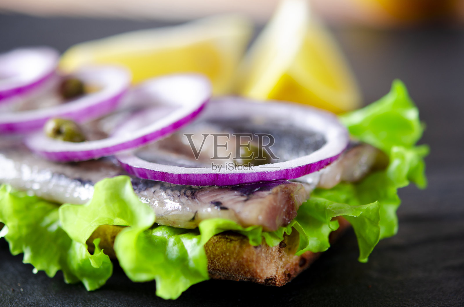 美味的挪威鲱鱼,莴苣,蓝洋葱,柠檬和西红柿放在木板上照片摄影图片