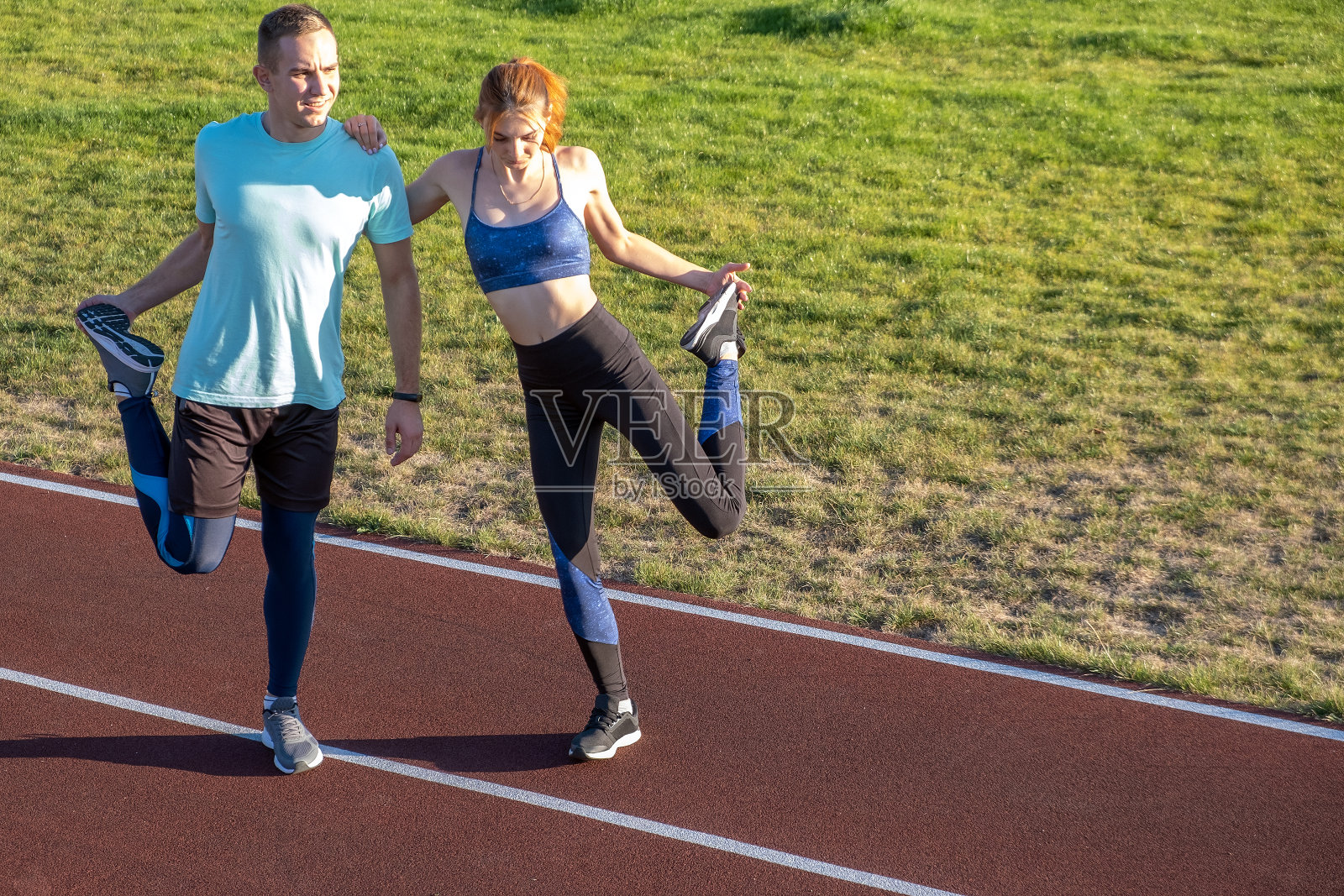 年轻的一对健康的运动员男孩和女孩做热身运动前跑在公共体育场的红色轨道户外。照片摄影图片
