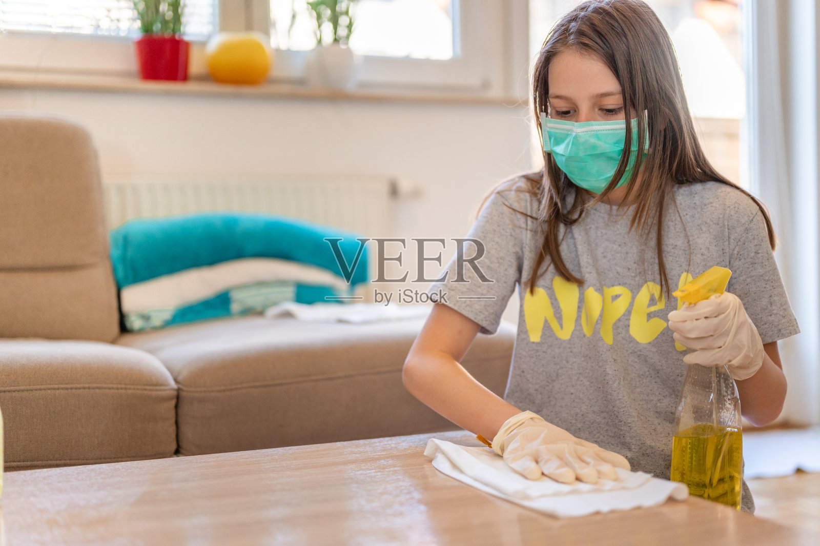 年轻女孩戴着防护面罩和防护手套在家清洁桌子照片摄影图片