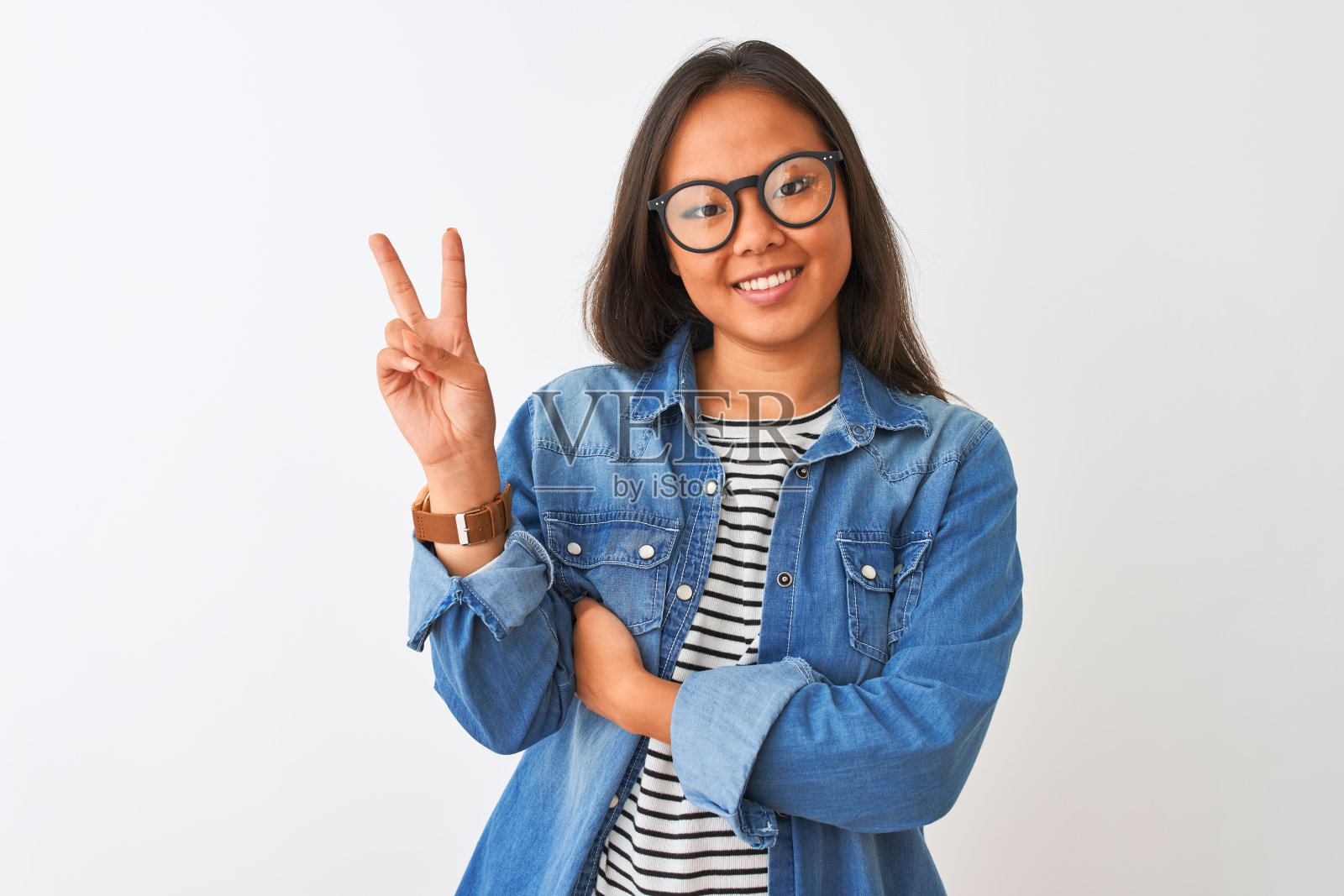 年轻的中国妇女穿着牛仔衬衫和眼镜在孤立的白色背景微笑着,快乐的脸对着镜头眨着眼睛做胜利标志。二号人物。照片摄影图片