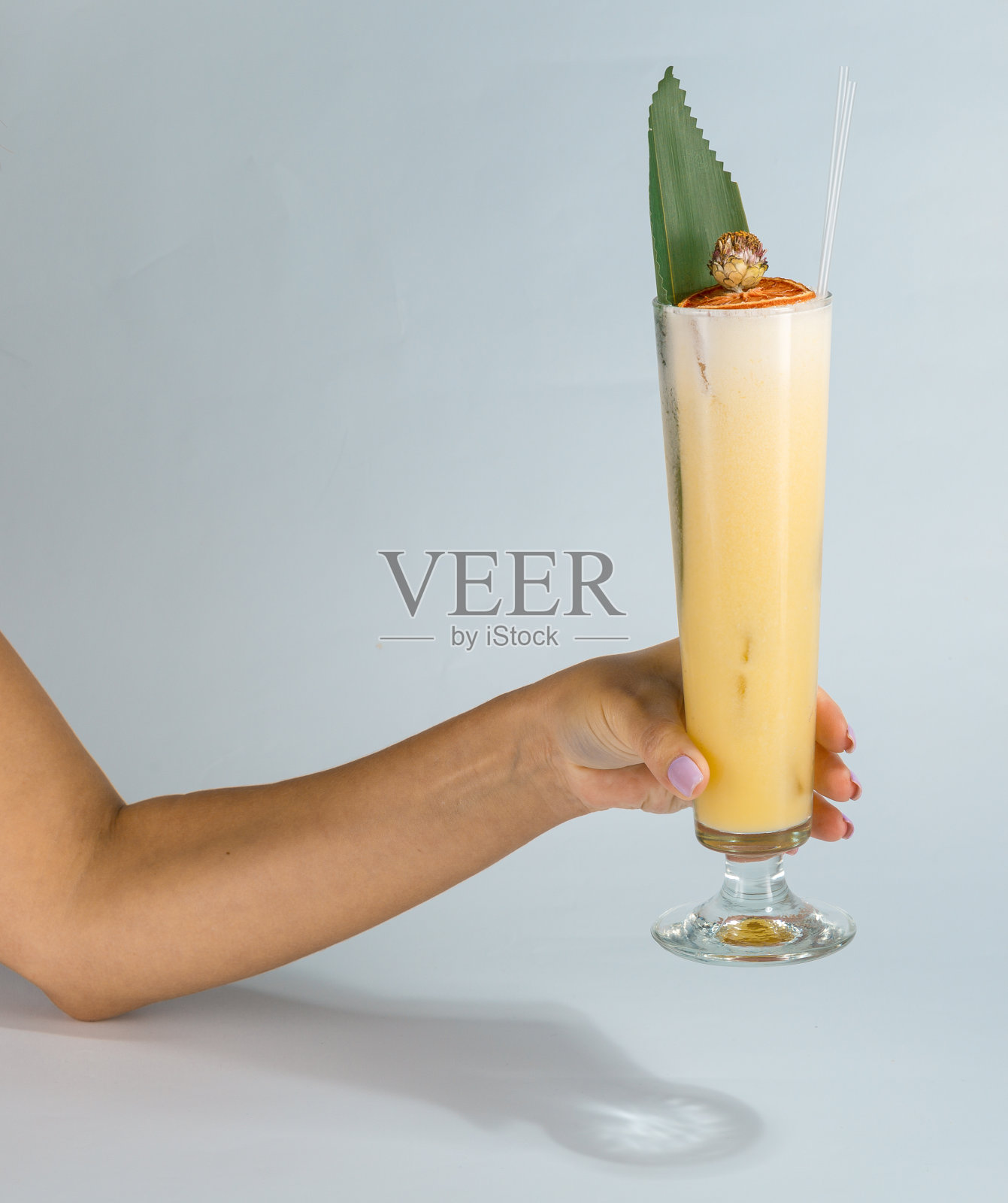 一个女人的手拿着一杯热带菠萝朗姆酒鸡尾酒在白色的背景与复制空间的特写。暑期度假概念。照片摄影图片
