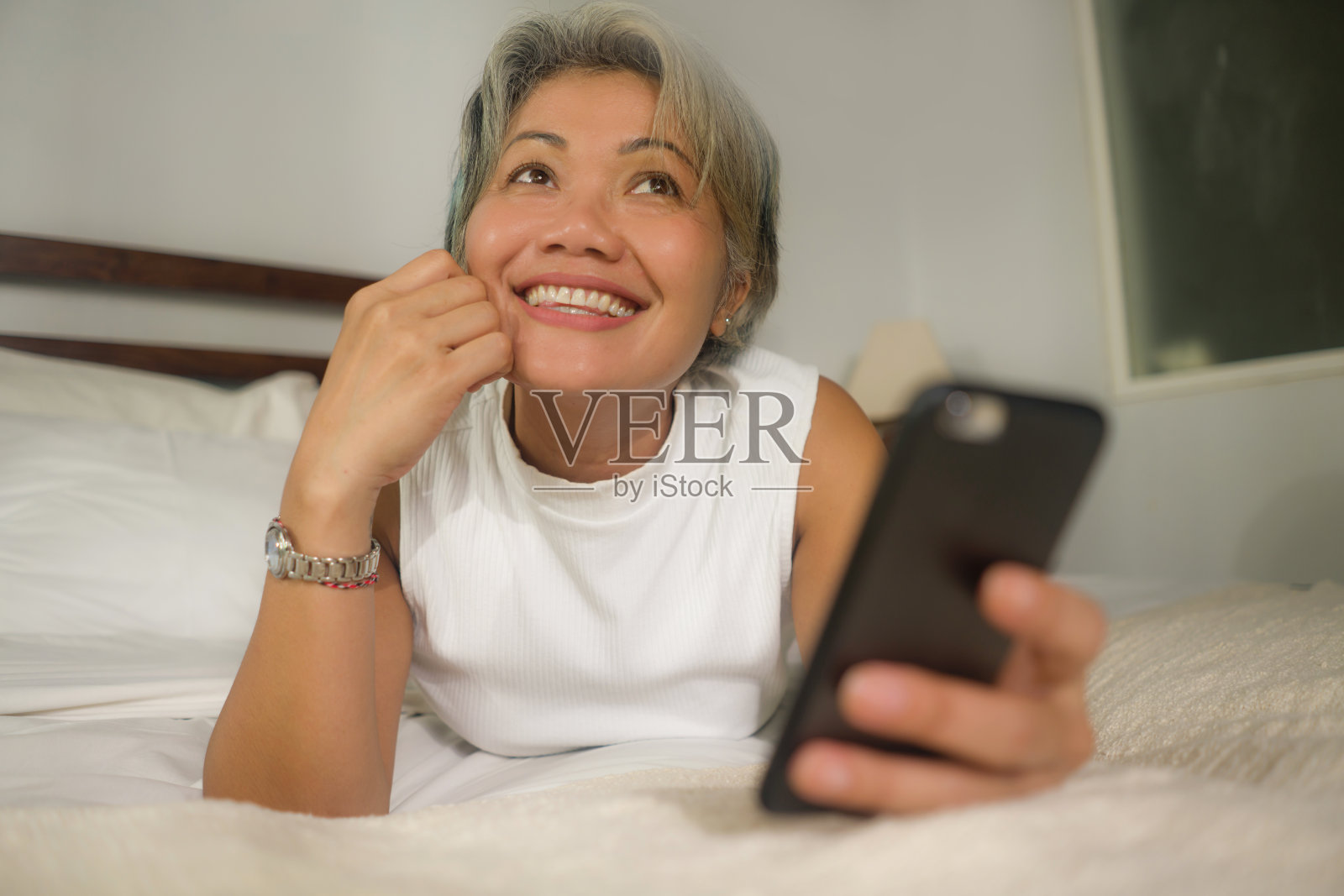 家庭生活方式肖像有吸引力和快乐的中年妇女在她的50多岁使用互联网手机在床上放松和愉快的在线约会或享受社交媒体应用程序照片摄影图片