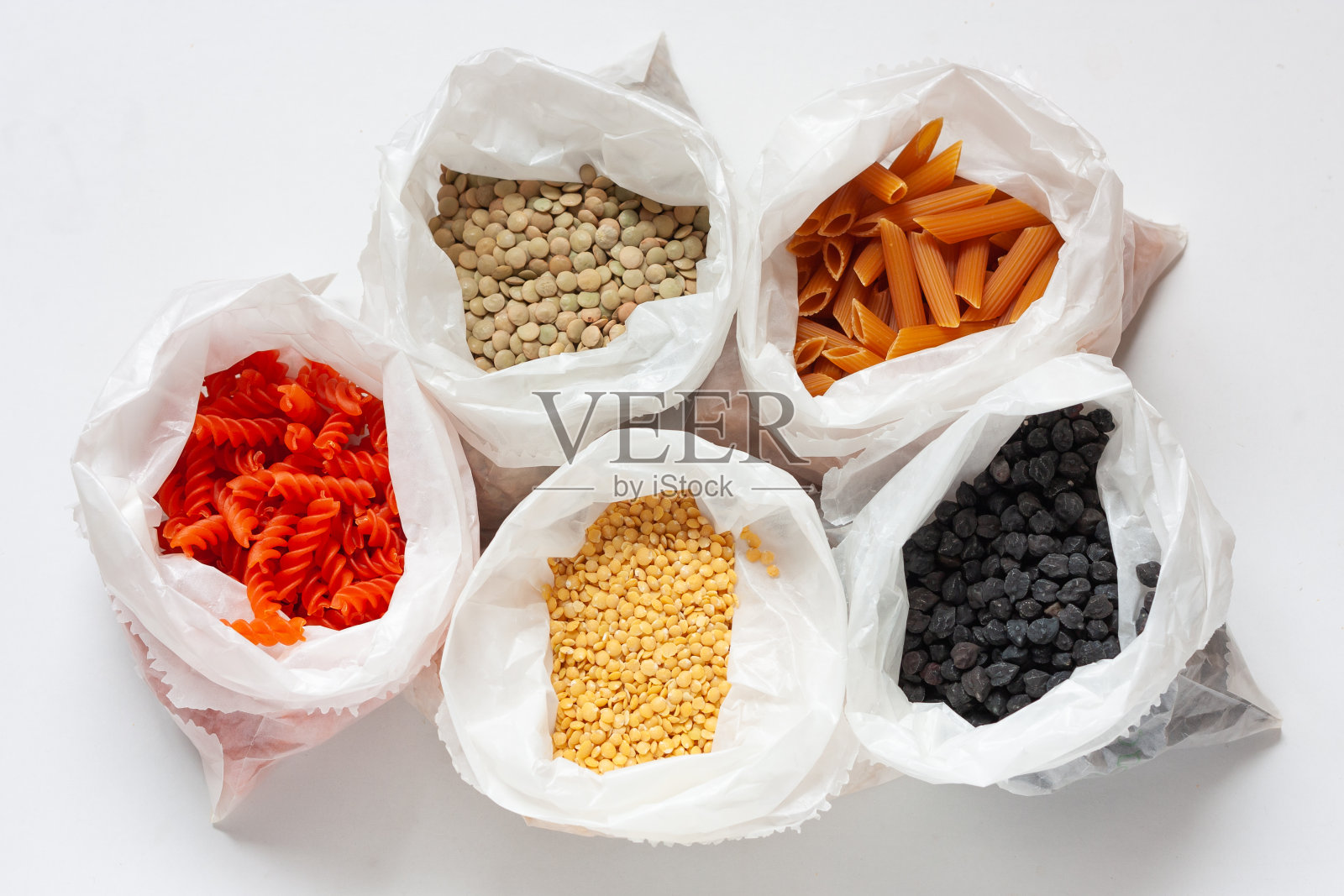 几粒豆荚和豆荚糊在纸袋上白色的背景。红色和黄色的小扁豆糊,绿色和黄色的小扁豆,黑色的鹰嘴豆。植物蛋白。前视图。照片摄影图片