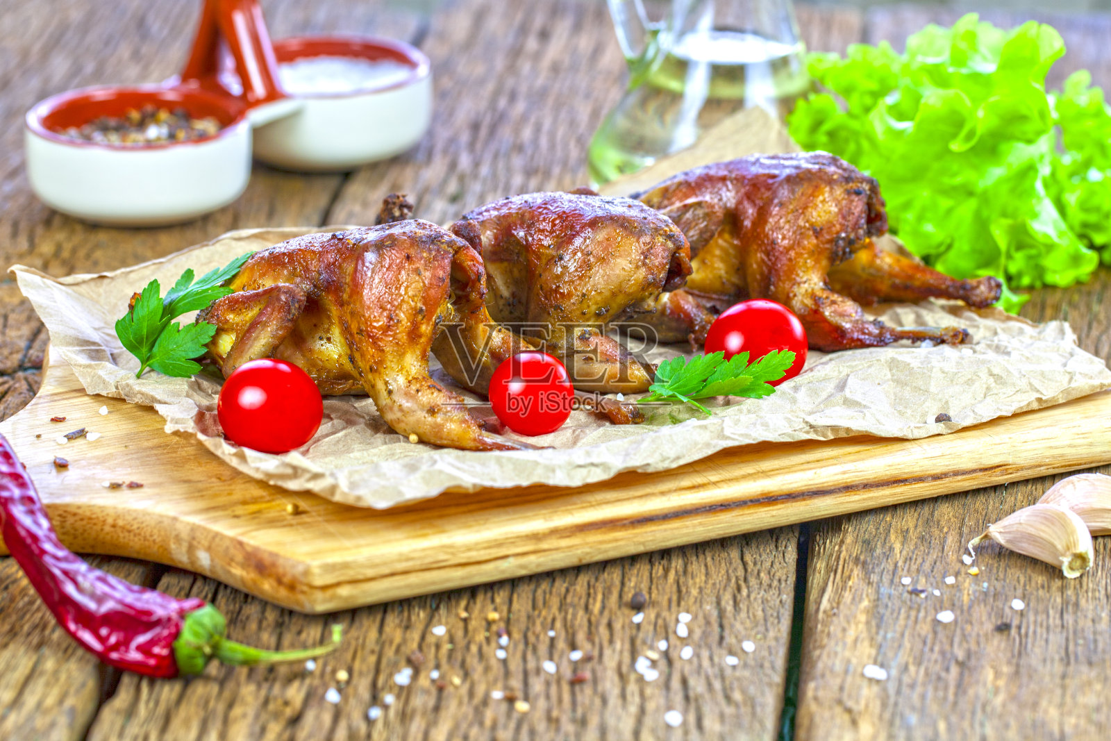 晚餐。烤鹌鹑尸体,橙子,西红柿,新鲜欧芹和一杯葡萄酒放在木桌上,照片摄影图片