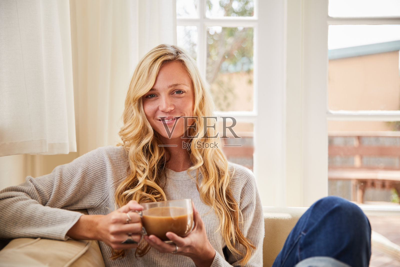 微笑的年轻女子在她的客厅沙发上喝咖啡照片摄影图片