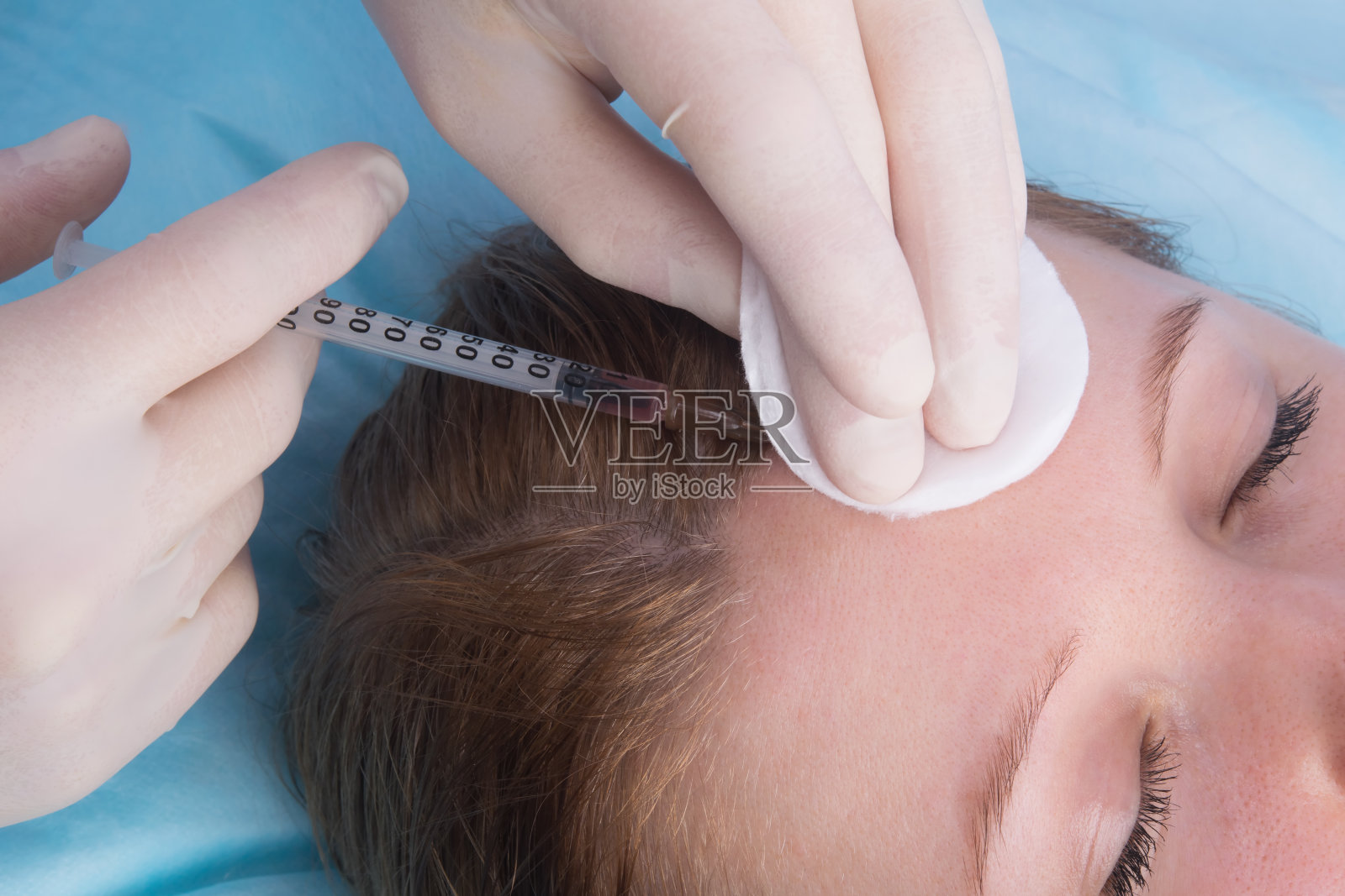 美容,双手戴无菌手套,给一个闭着眼睛的女人做美容注射,在额部,特写照片摄影图片