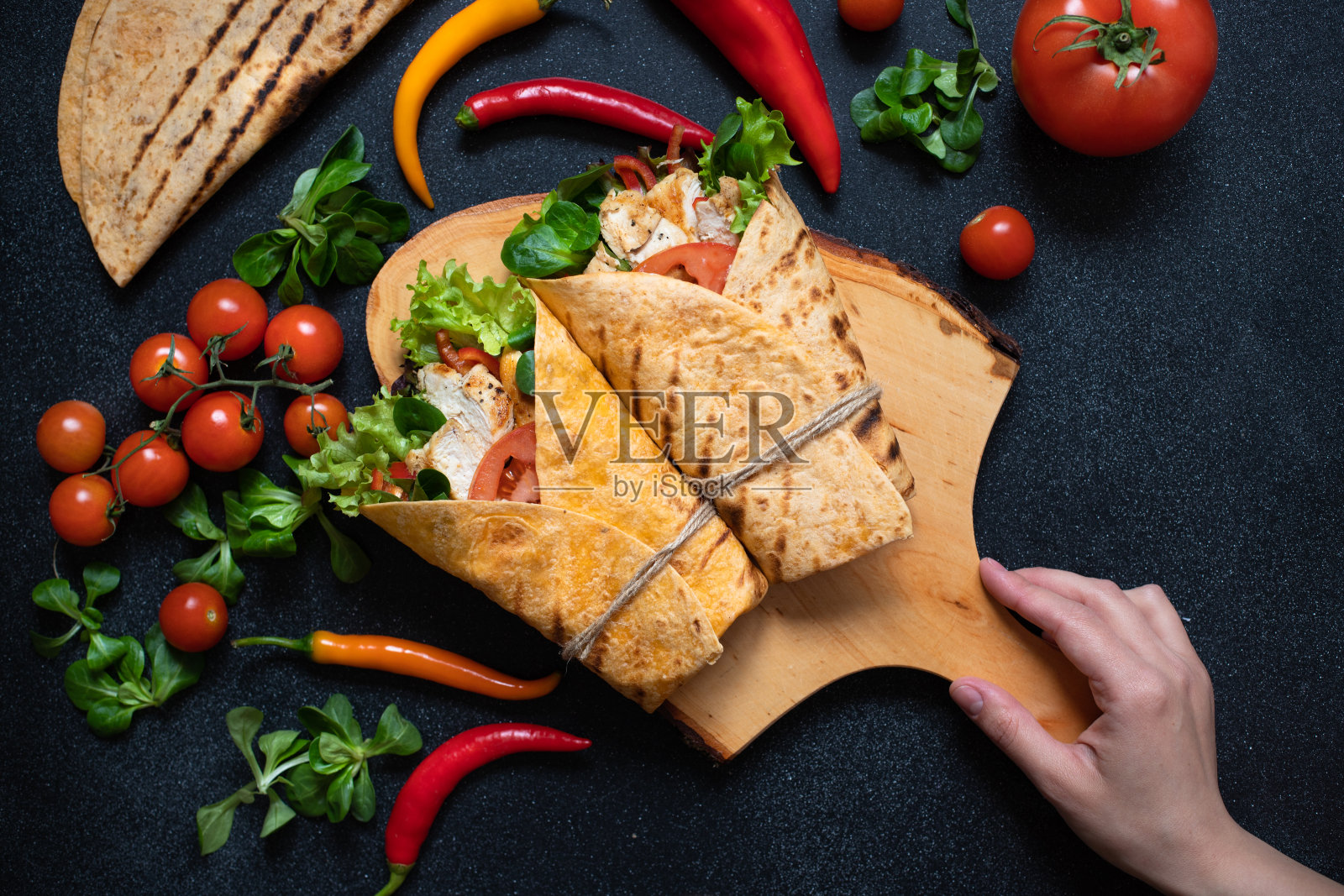 墨西哥玉米粉圆饼与烤鸡和新鲜蔬菜包裹在木制砧板上。饮食健康的菜肴。黑色背景,平铺,复制空间照片摄影图片