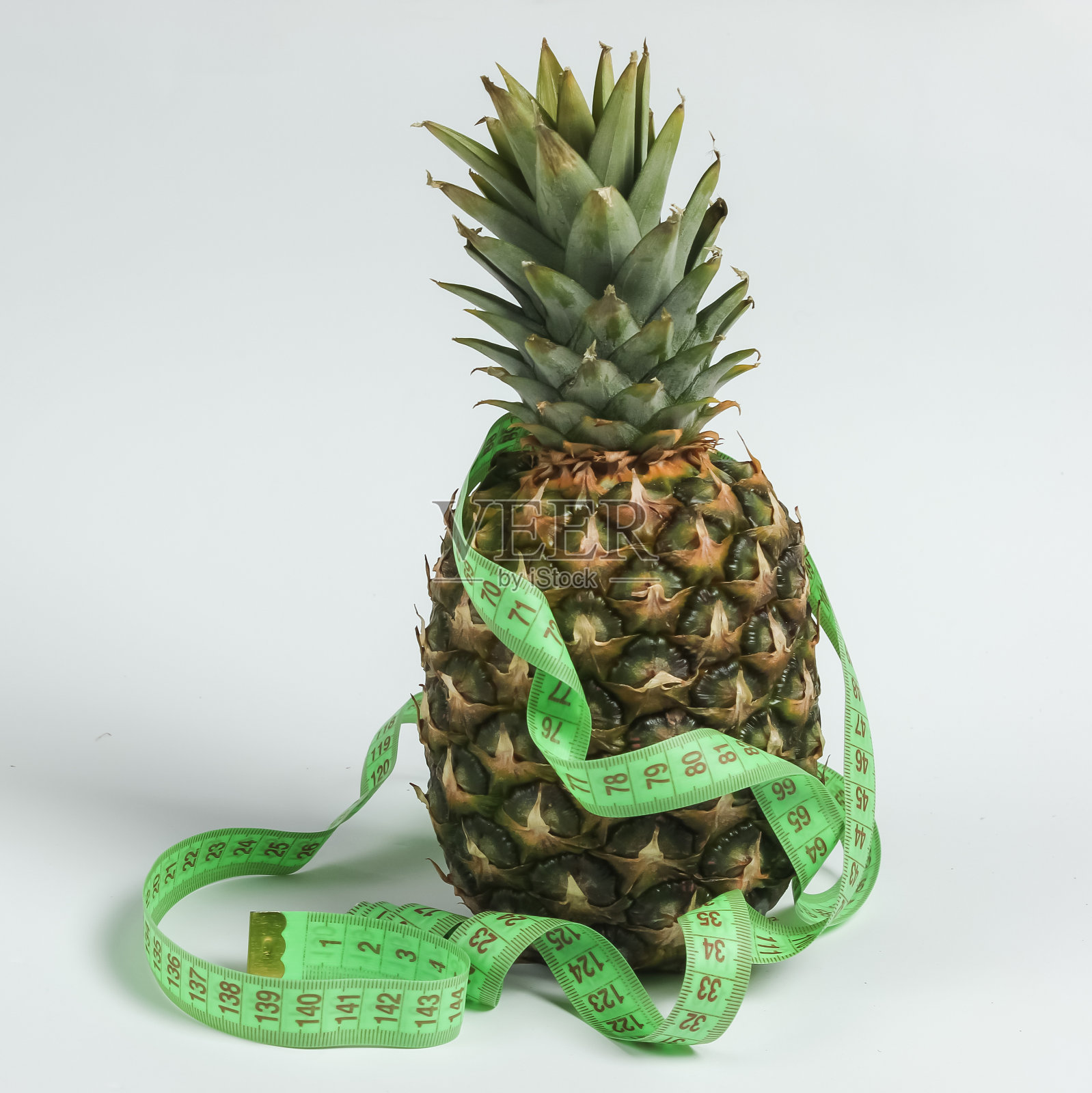减肥的概念。水果的饮食。白色背景上,用卷尺包着的菠萝照片摄影图片