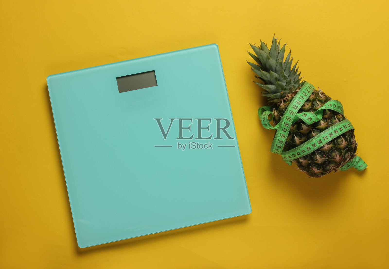 减肥的概念。鳞片,菠萝用卷尺包裹在黄色的背景上。健康饮食照片摄影图片
