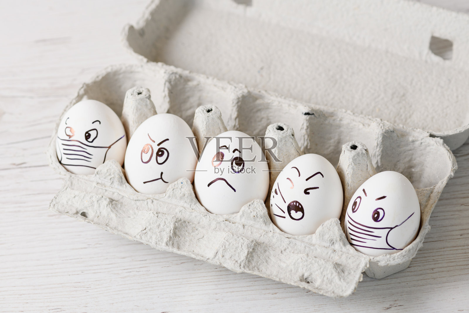 盒子里有带着医用口罩的涂鸦脸的鸡蛋。照片摄影图片