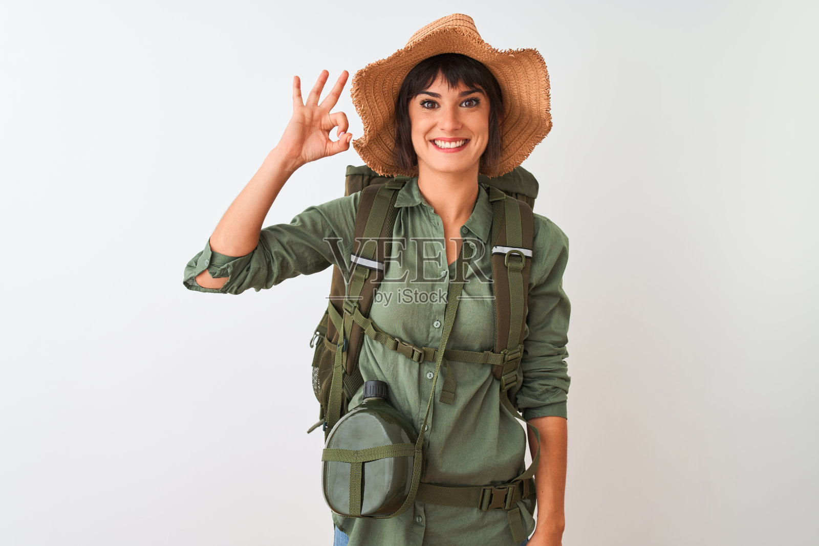 徒步妇女戴双肩包帽子和水水壶在孤立的白色背景微笑积极做ok手势与手和手指。成功的表达。照片摄影图片