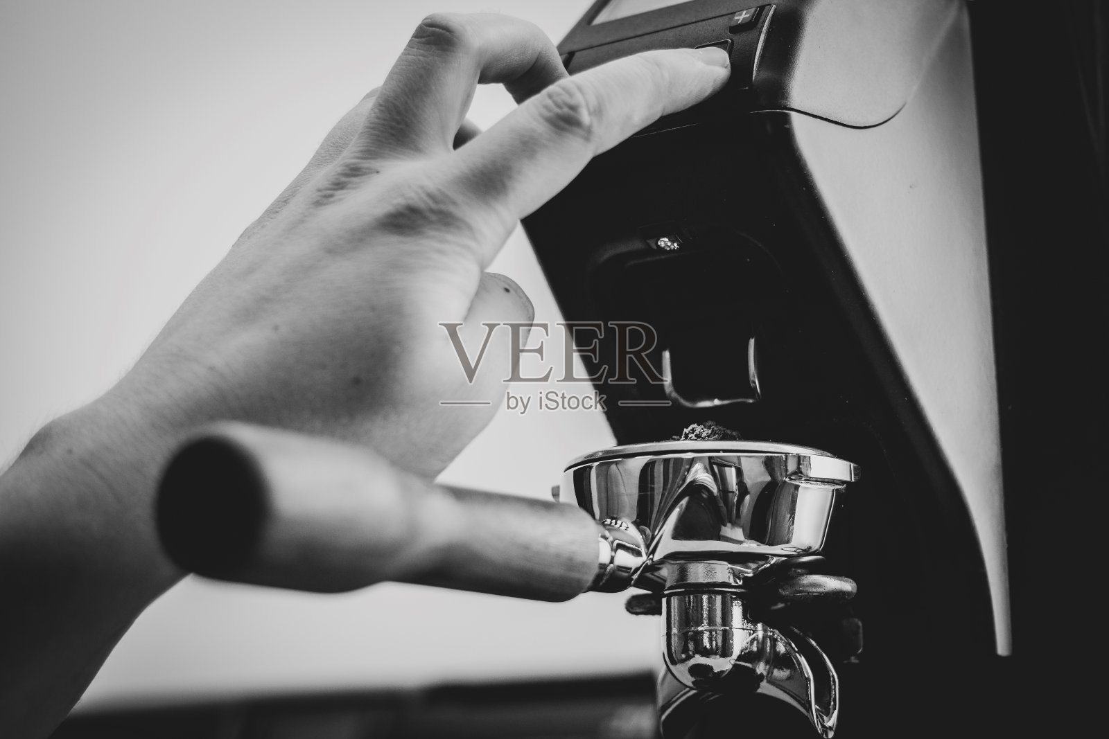 这是一幅咖啡师按下咖啡研磨机的按钮,将新鲜咖啡豆中的新磨成的咖啡渣倒入过滤机的肖像。照片摄影图片