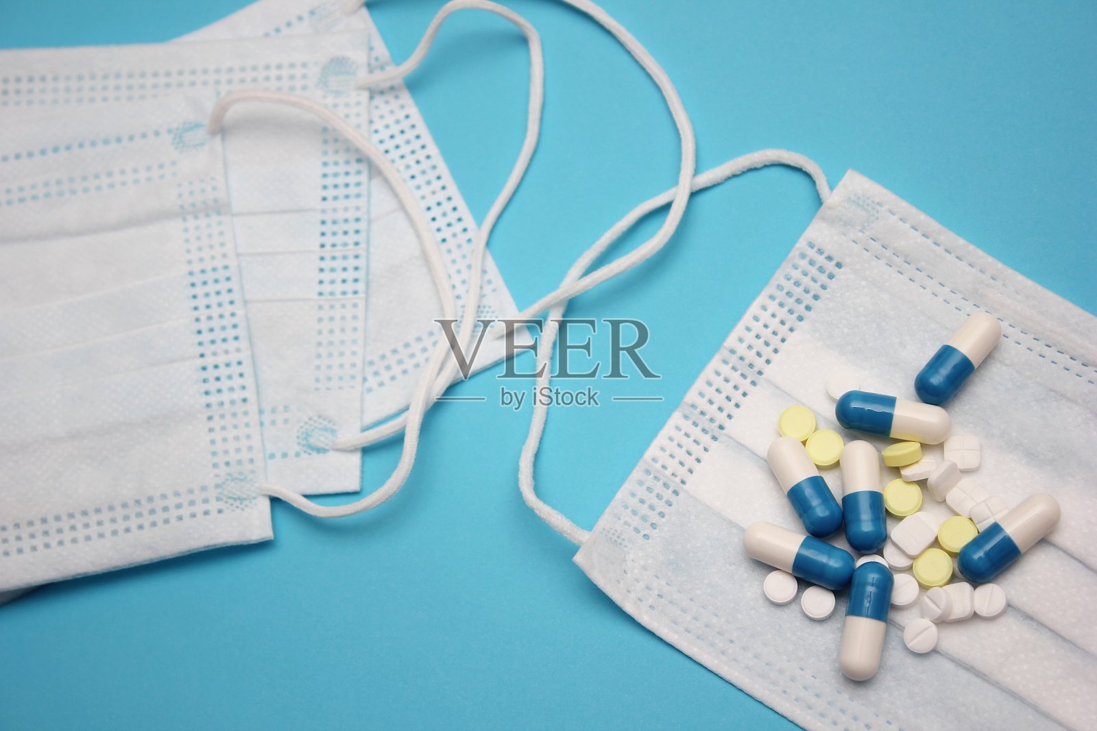 一个医用口罩,上面有很多药丸,还有蓝色的背景。照片摄影图片