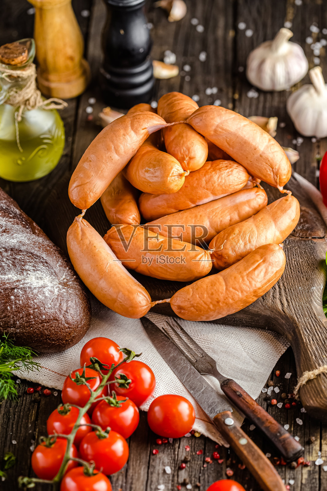 木质的乡村背景,多汁的新鲜香肠躺在砧板上,黑面包和西红柿,一刀一叉,最上面的镜头照片摄影图片