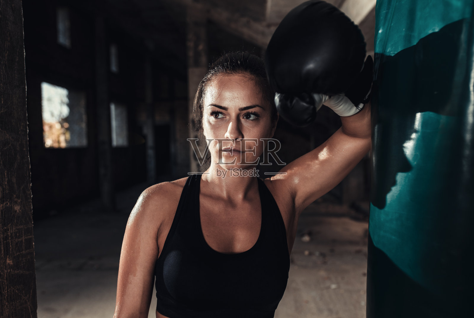 女拳击手在仓库里打了一个拳击袋后正在休息。照片摄影图片
