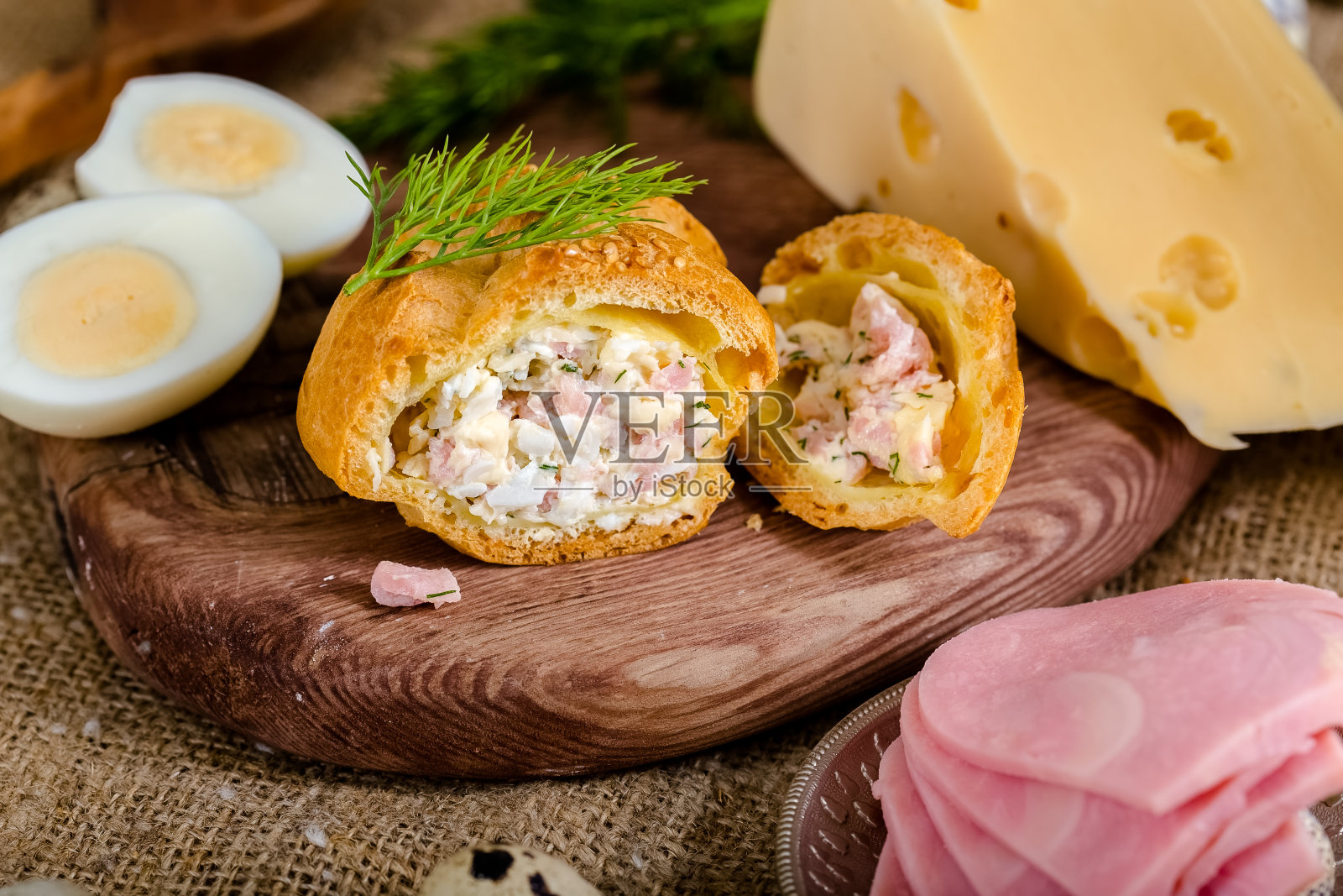 新鲜的小圆饼放在一个老式的木板上,培根,鹌鹑蛋,硬切达奶酪,煮鸡蛋,新鲜的绿色蔬菜,欧芹,麻布布上照片摄影图片