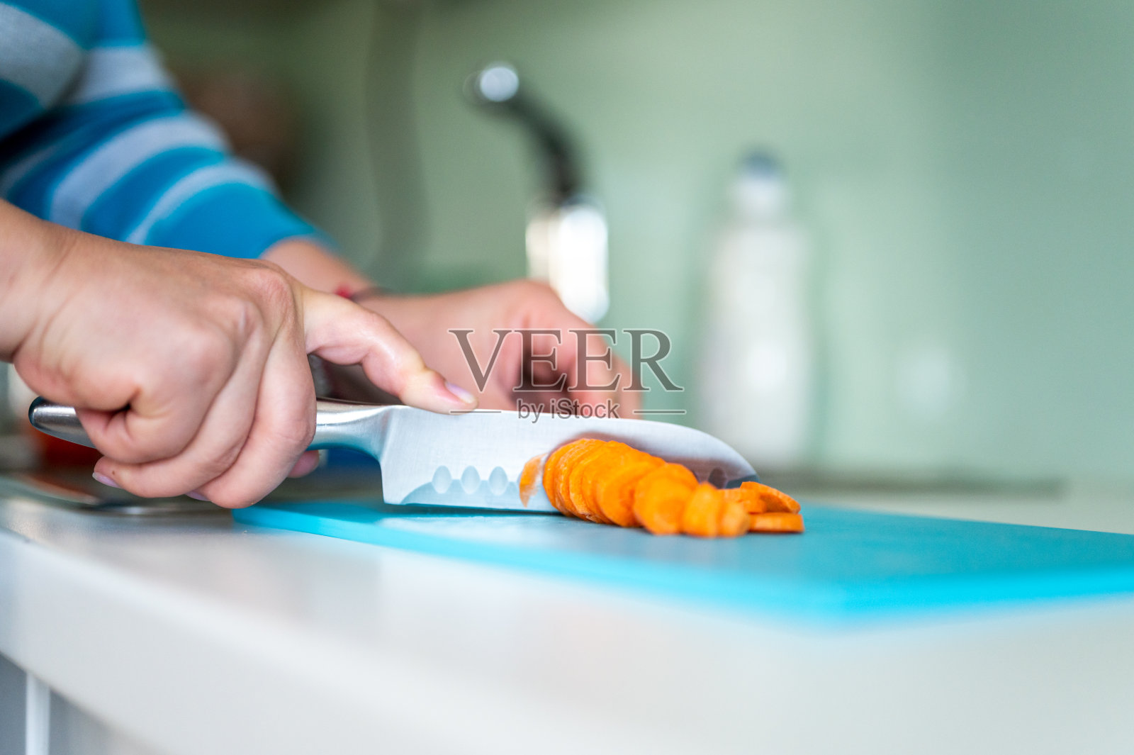 女性的手切胡萝卜在绿松石砧板上的特写照片摄影图片