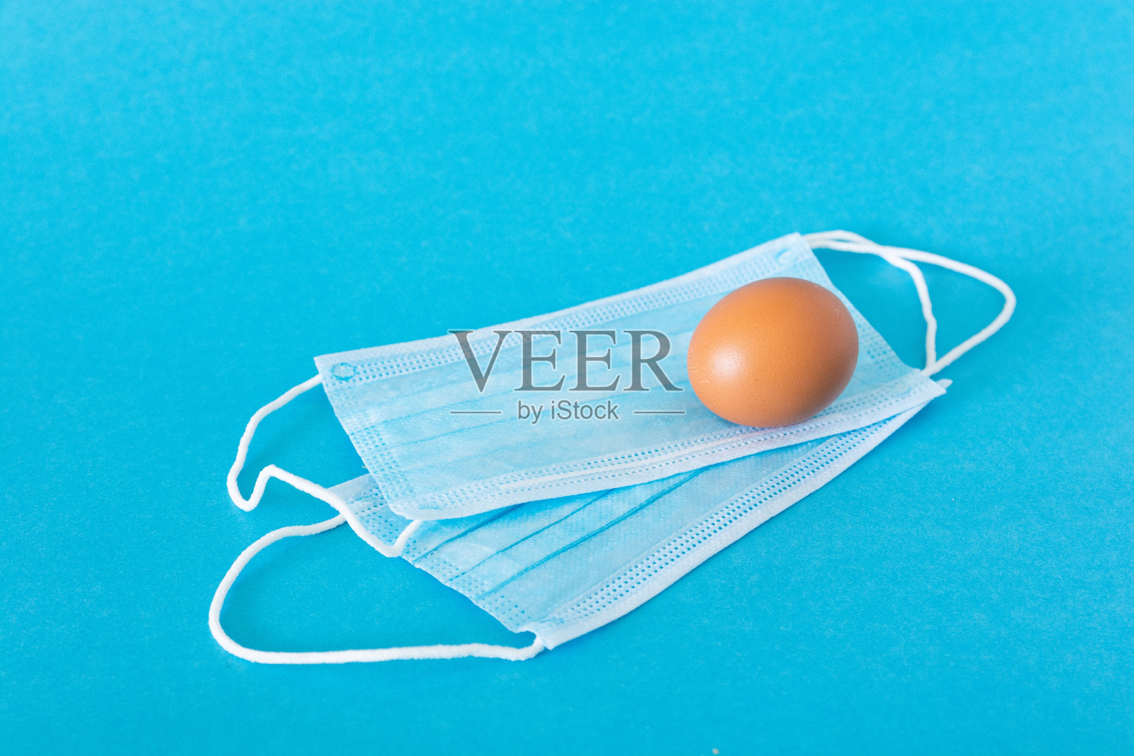 鸡蛋躺在脸上保护面罩,蓝色背景照片摄影图片