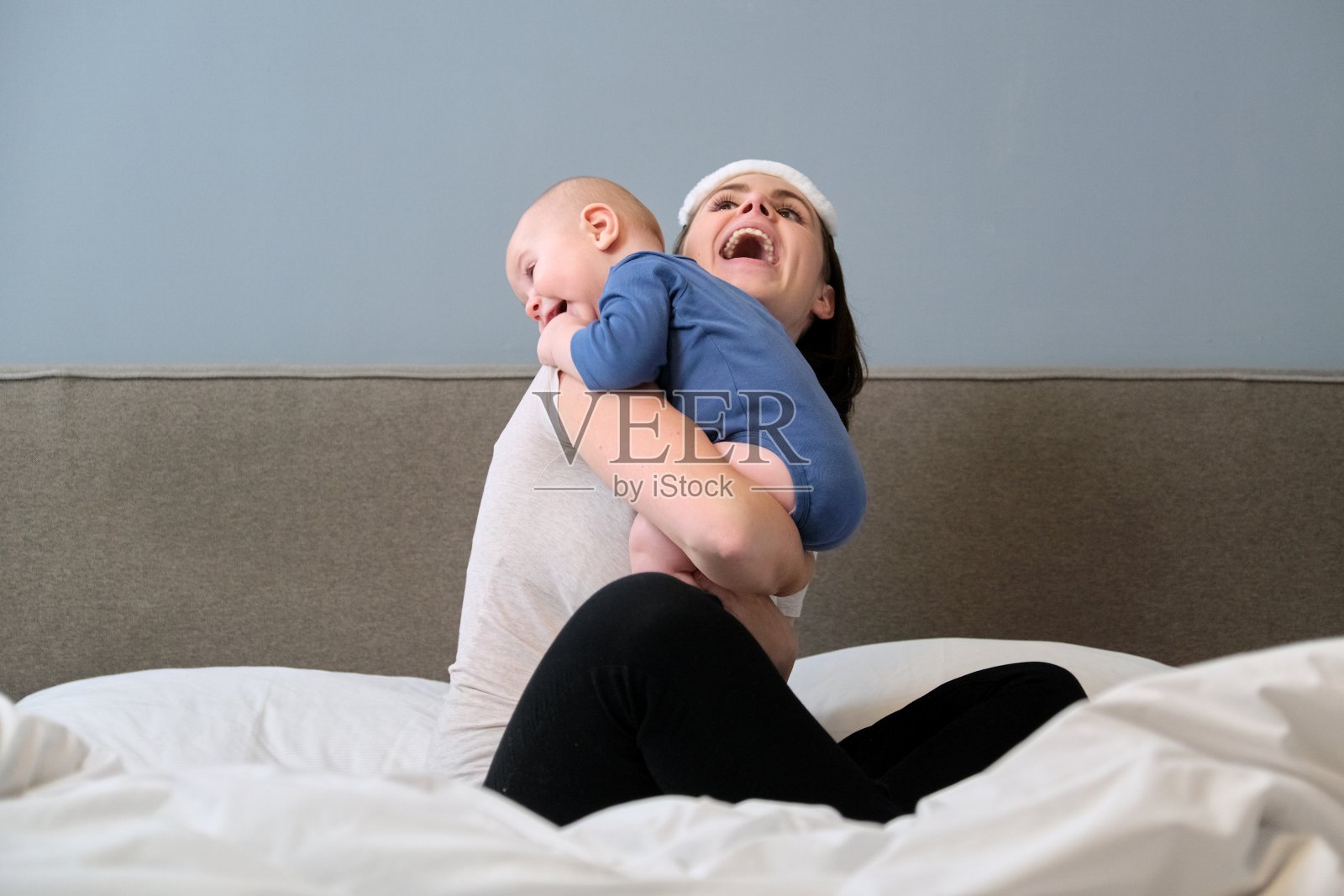 年轻的妈妈和宝宝一起坐在家里的床上照片摄影图片