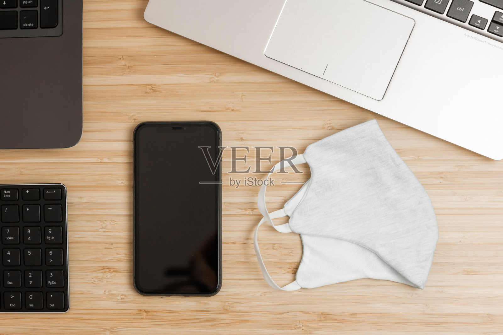 桌上放着一个防护口罩、一部智能手机和一台笔记本电脑。新冠肺炎疫情期间的工作场所组织照片摄影图片