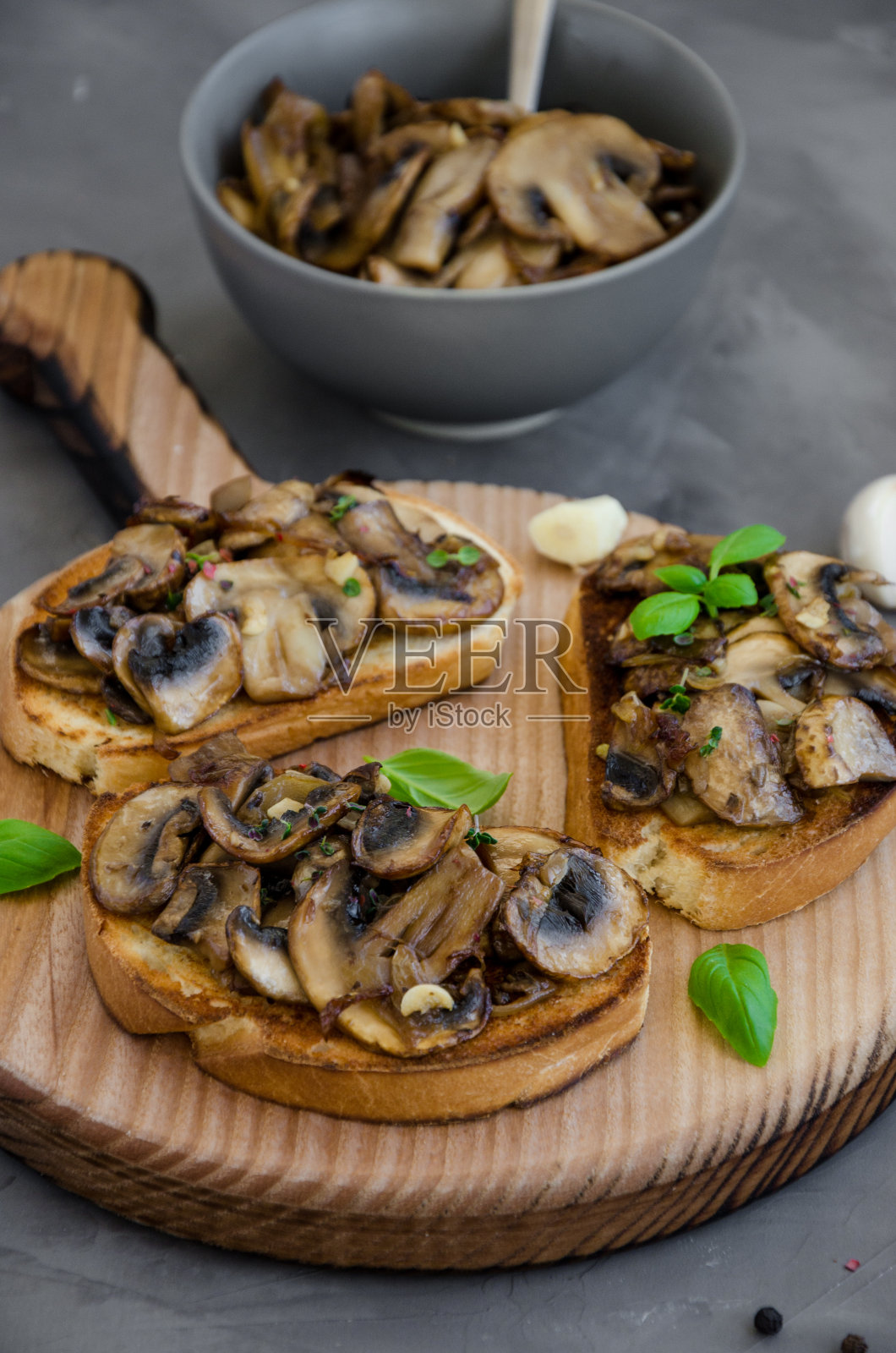 意式烤面包配炸蘑菇,洋葱,大蒜,百里香和罗勒,放在切菜板上,背景是深色混凝土。垂直方向。关闭了。照片摄影图片