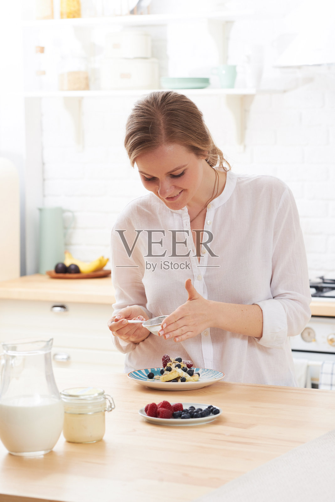 在清晨的阳光下,快乐的年轻女子在厨房的餐桌上准备美味的小吃照片摄影图片