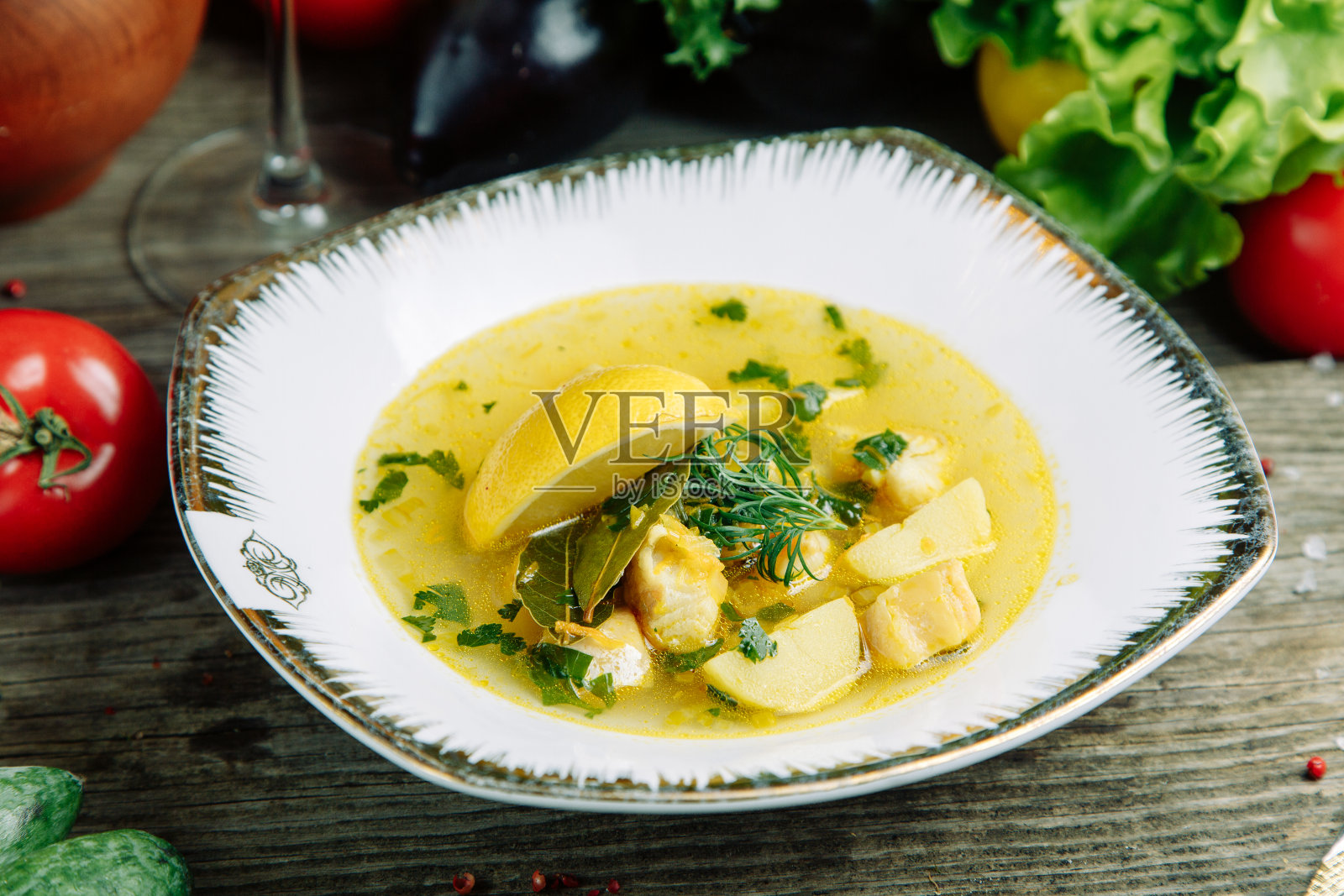 一盘有鱼、海鲜和柠檬的汤。餐厅菜肴在木背景与蔬菜。照片摄影图片