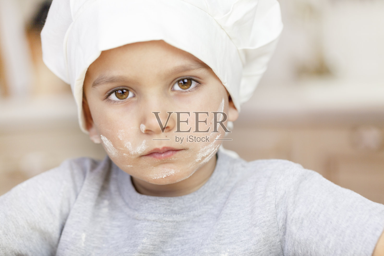 年轻的厨师,一个男孩的肖像戴着厨师帽,他的脸上带着悲伤的表情,他的脸上涂着面粉,色调照片摄影图片