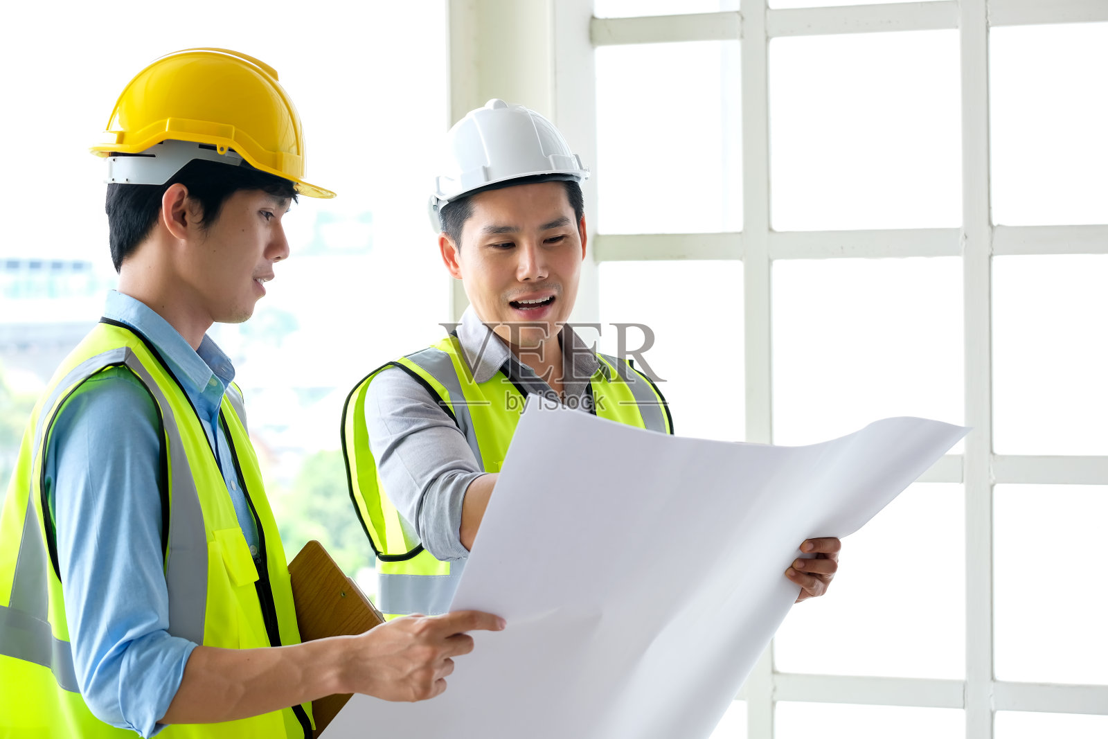 两名工程师站在工地前。左边工程师拿着蓝图图照片摄影图片