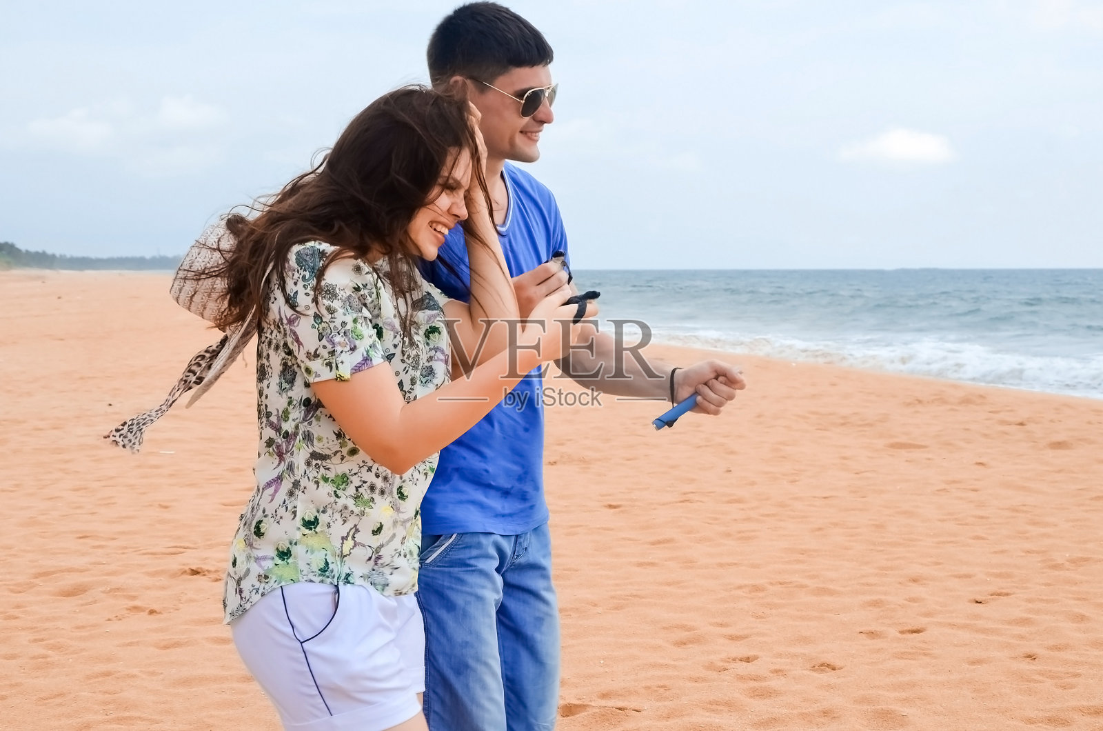 一个拿着相机的黑发男人和一个穿着白色短裤的黑发女孩在沙滩上散步。快乐的小夫妻手捧海龟,志愿者拯救并放生海龟到海里。海洋保护研究中心。照片摄影图片