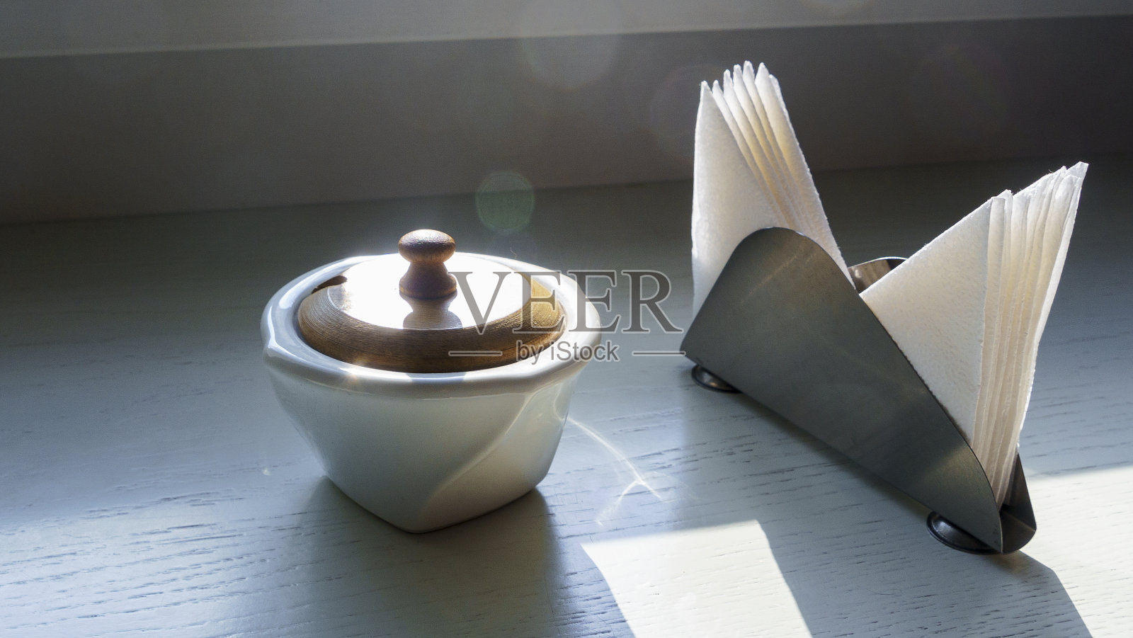 白色的桌子上放着白糖碗和餐巾架,被明亮的阳光照射着。空间的文本。照片摄影图片