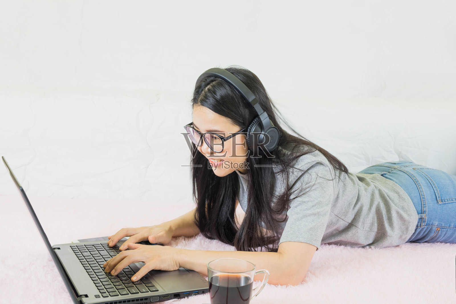 年轻美丽的亚洲女人穿着灰色t恤和牛仔裤,躺在客厅的粉红色地毯上,在线工作的生活方式,放松在家里的咖啡杯,在家工作笔记本电脑,在家工作照片摄影图片